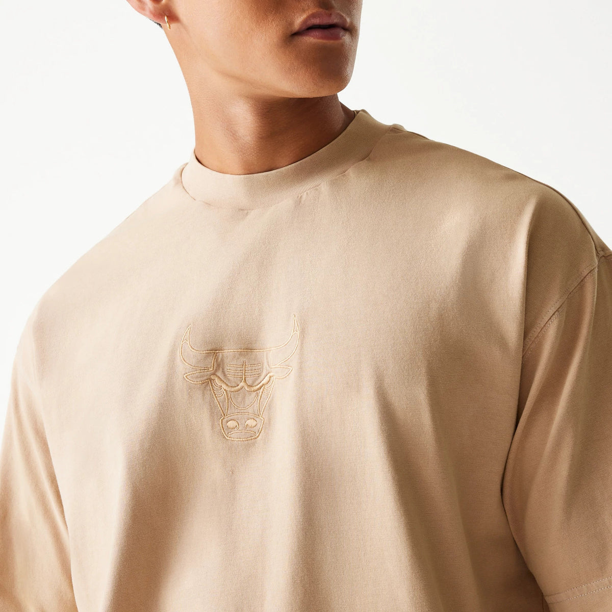 New Era Chicago Bulls NBA Washed Beige Box T-Shirt, on-model view showing the beige fabric with an embossed Bulls logo centred on the chest, close to the neckline and short sleeves extending outwards.