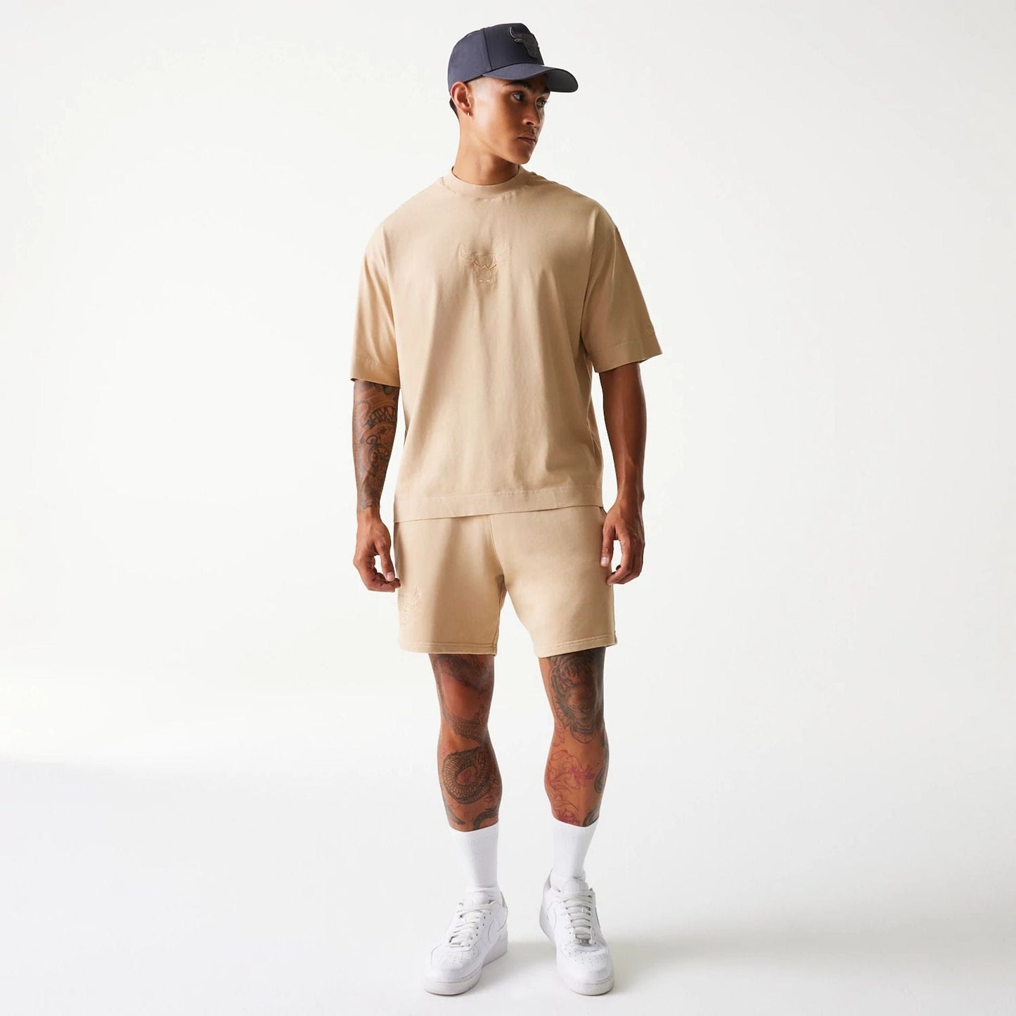 New Era Chicago Bulls NBA Washed Beige Box T-Shirt, on-model view showing the round-neck beige T-shirt with short sleeves, a debossed Chicago Bulls logo on the chest, paired with matching shorts and a purple cap.