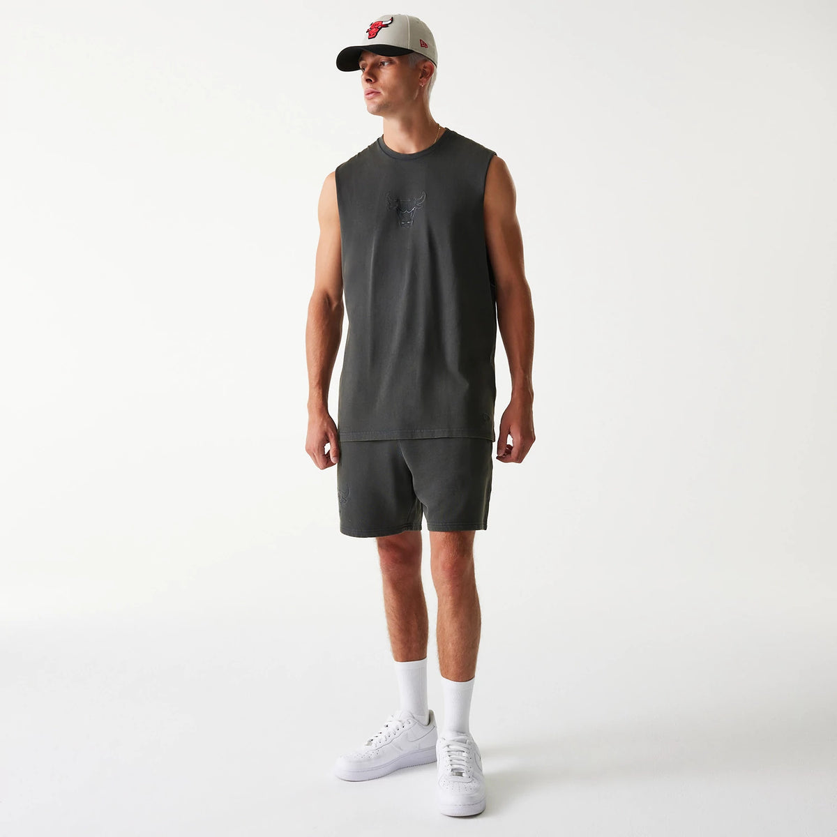 New Era Chicago Bulls NBA Washed Grey Shorts, on-model view showing the grey shorts worn with a matching sleeveless top, featuring an embossed Chicago Bulls logo on the left leg and complemented by a grey cap with a Bulls emblem.