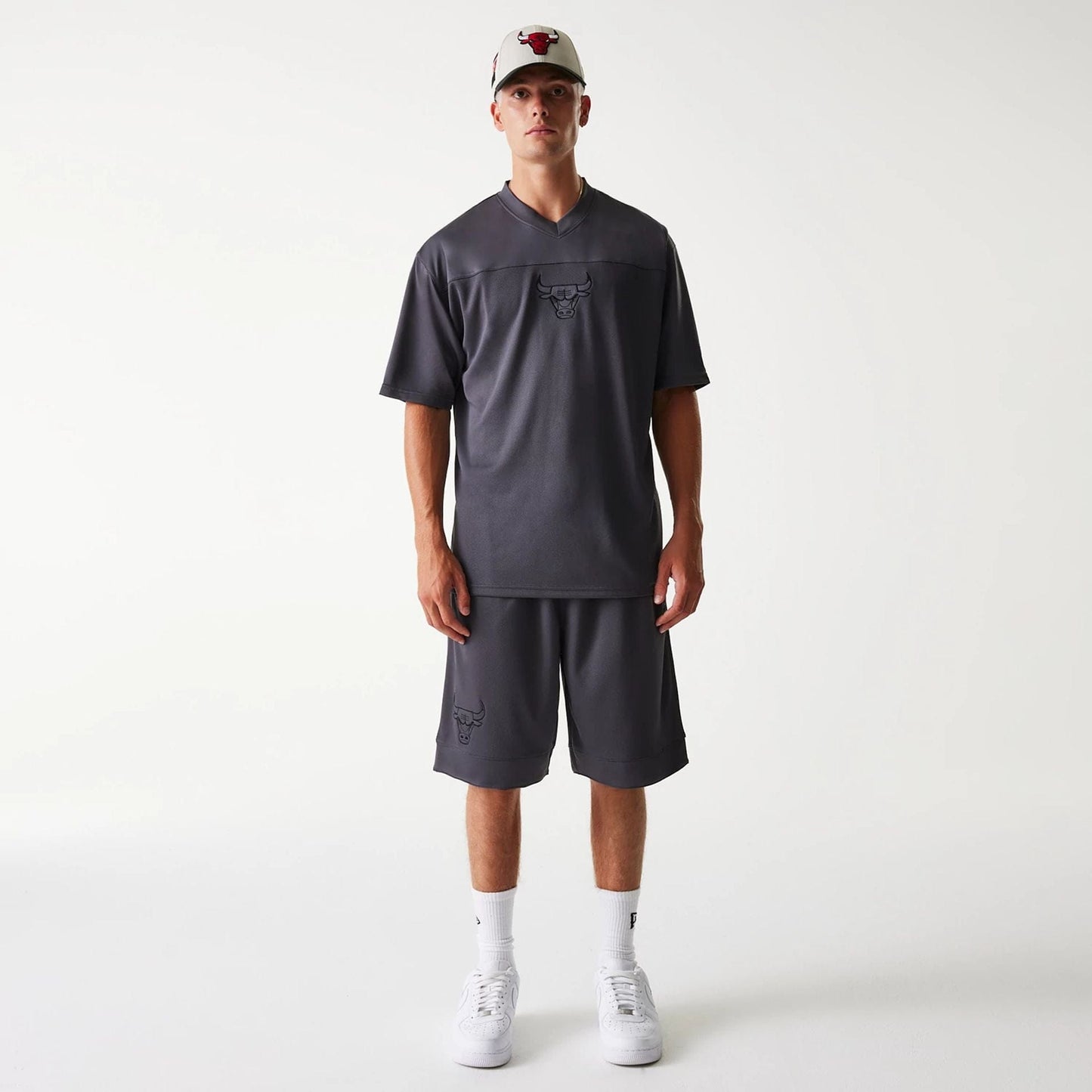 New Era Chicago Bulls NBA Tonal Dark Grey Mesh Shorts, on-model view showing the relaxed fit shorts with a raised Chicago Bulls logo near the hem, paired with a matching dark grey top and a white cap featuring the Bulls emblem.