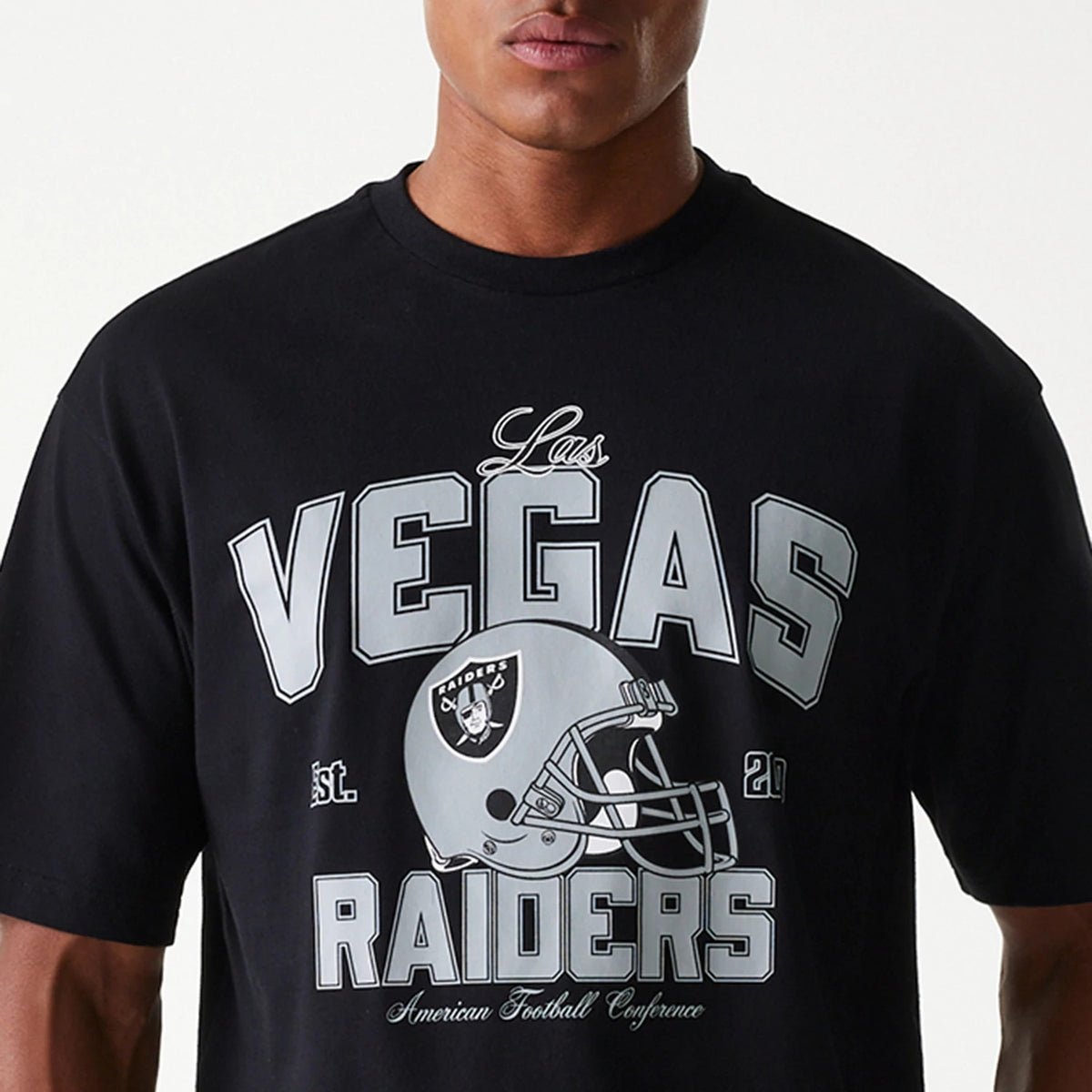 New Era Las Vegas Raiders NFL Helmet Black Oversized T-Shirt, front view showcasing a large grey print with Las Vegas Raiders text and a football helmet graphic on the chest, worn by an individual.