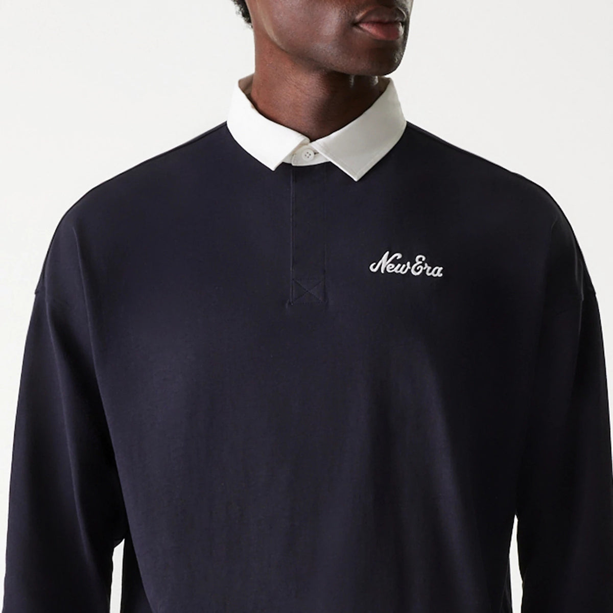 New Era Navy Oversized Rugby Shirt, front view on a model showing the white New Era script logo embroidered on the left chest, with a contrasting white collar and two-button placket against the dark navy fabric.