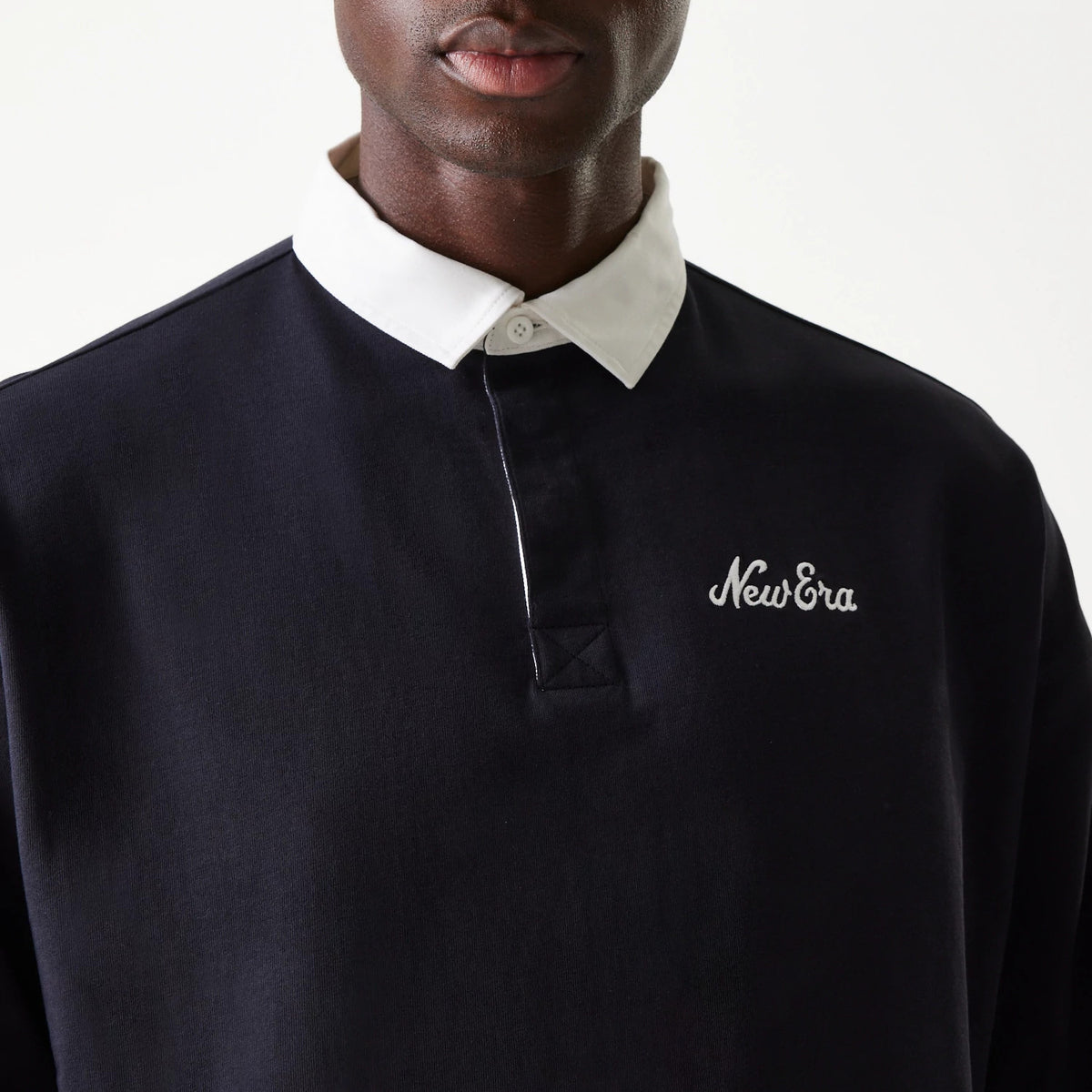 New Era Navy Oversized Rugby Shirt, close-up on-model with a white button-down collar, featuring an embroidered New Era logo on the left chest, highlighting the shirt's structured navy fabric.