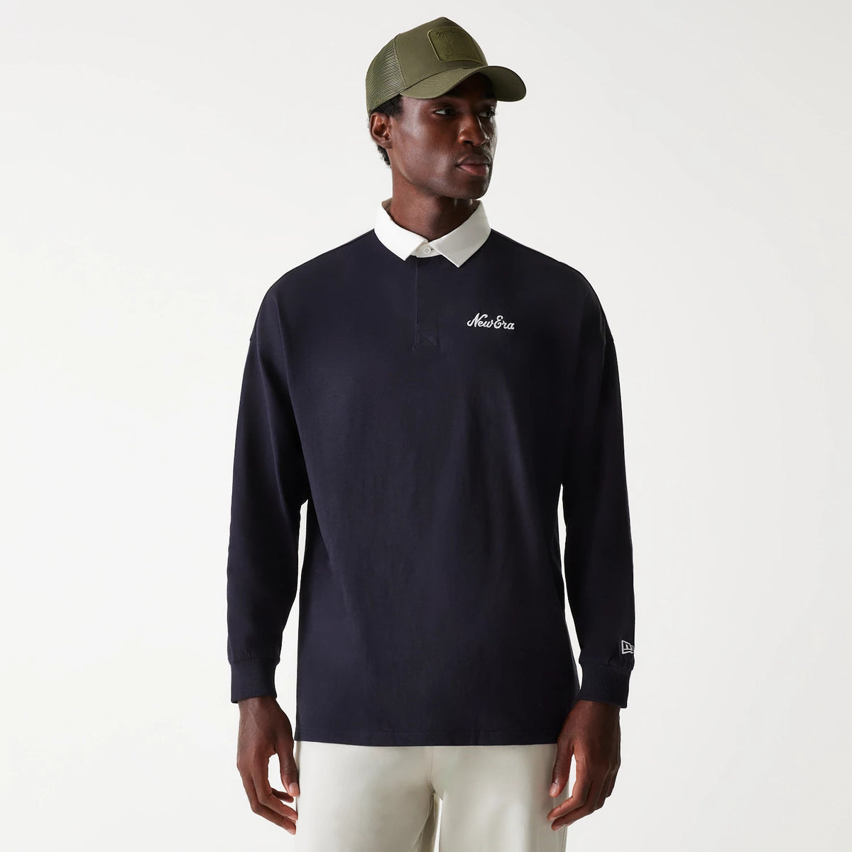 New Era Navy Oversized Rugby Shirt, front view on a model wearing a matching olive green cap, featuring white New Era embroidery on the chest and sleeve, with a contrasting white collar and long sleeves.
