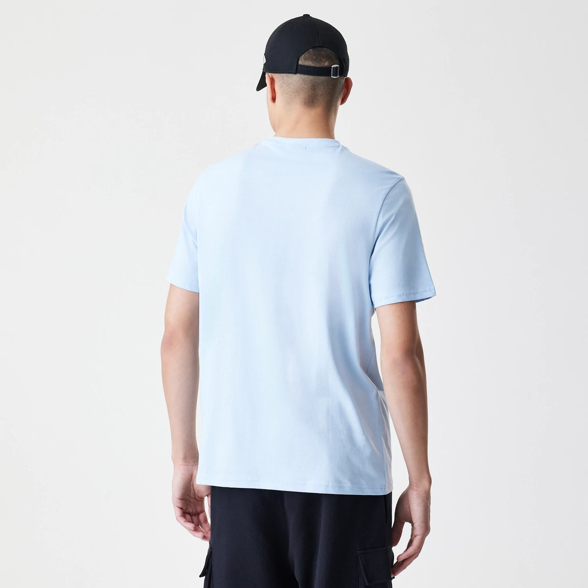 New Era LA Lakers NBA Bubble Wordmark Pastel Blue T-Shirt, rear view showing the plain pastel blue back of the T-shirt with short sleeves, worn by a person also wearing a black cap with a small debossed New Era logo on the side.