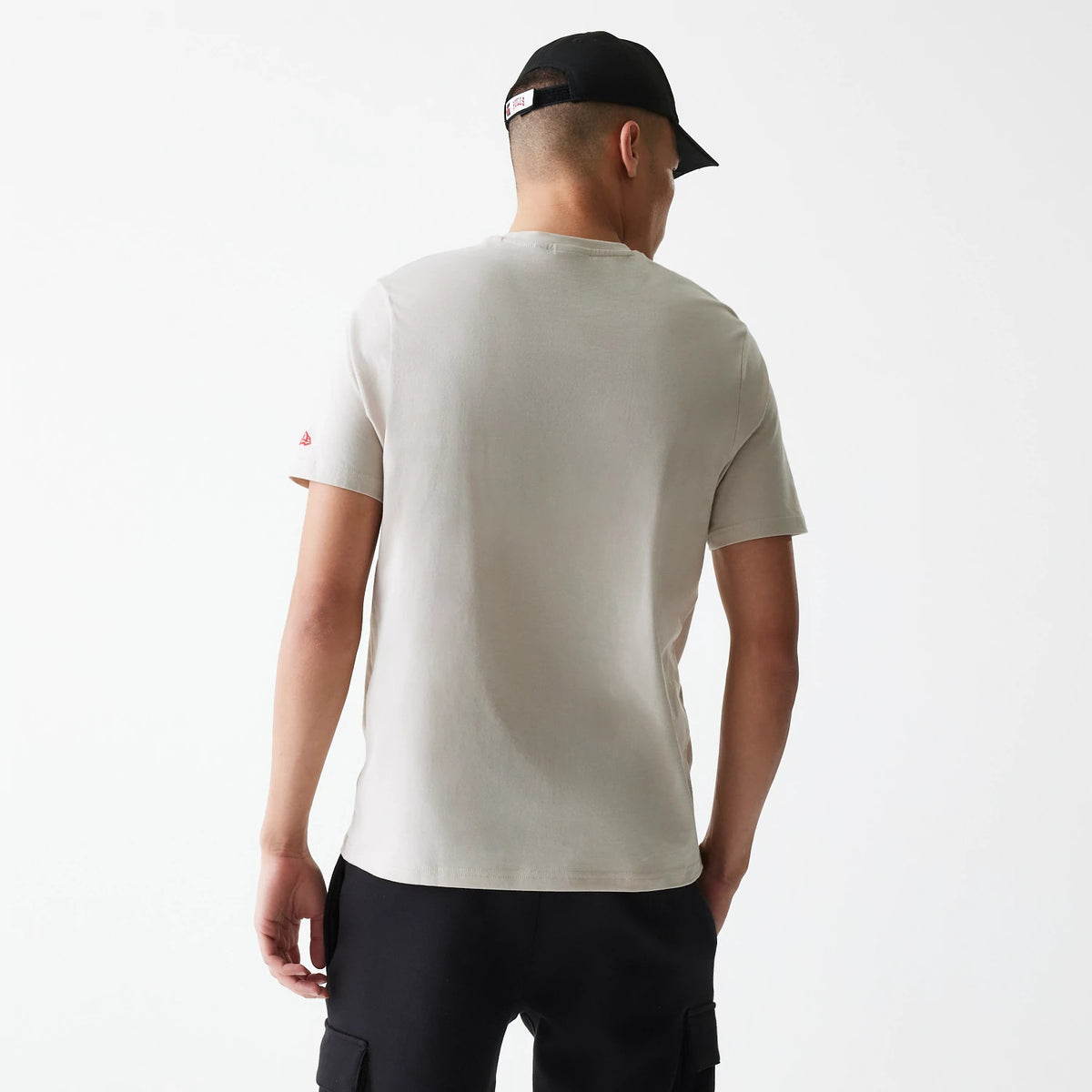 New Era Chicago Bulls NBA Logo Cream T-Shirt, rear view showing the plain cream back with a red embroidered logo on the left sleeve, a man wearing the T-shirt paired with black shorts and a black cap.