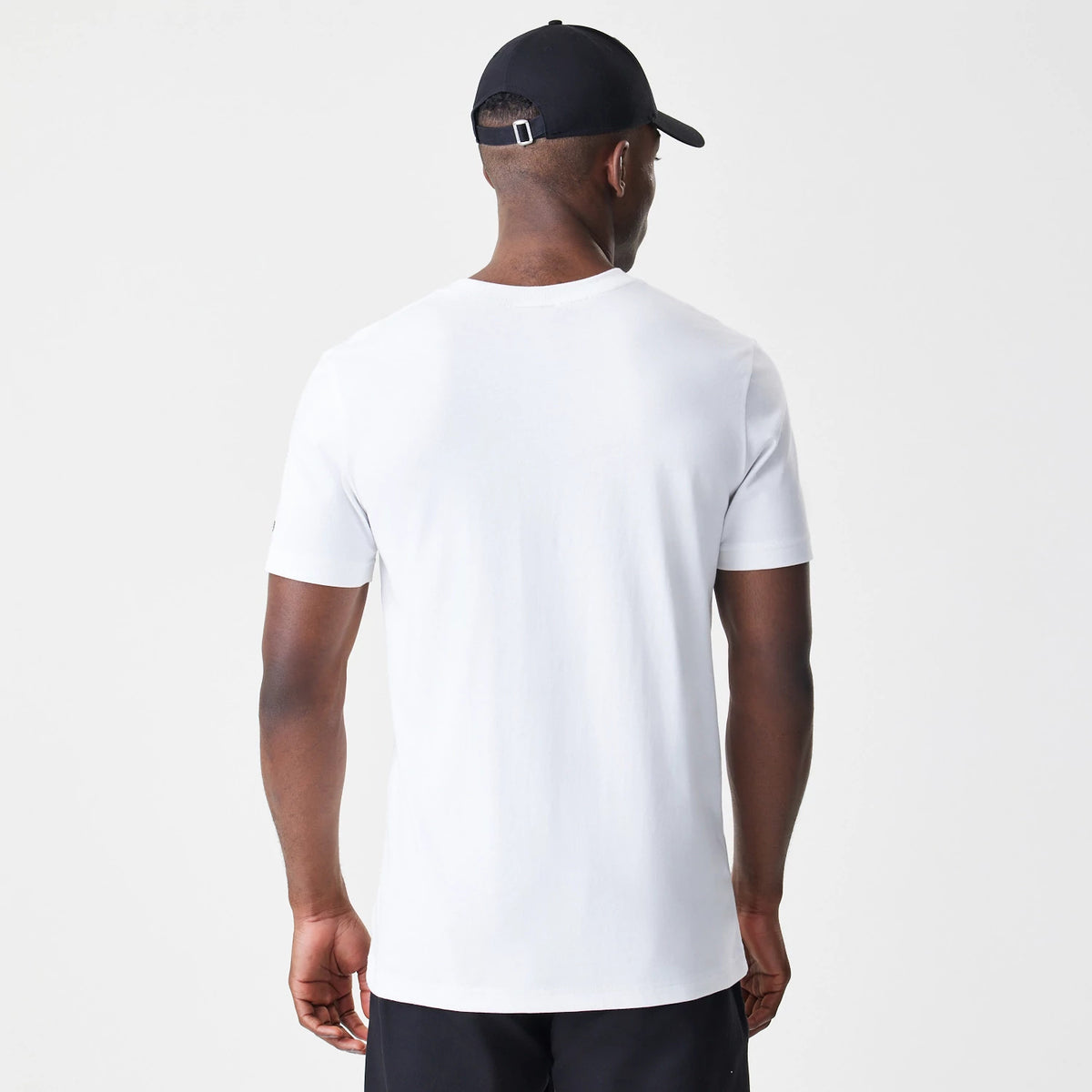 New Era Caddyshack Caddy Day Tournament White T-Shirt, rear view showing a plain white back with short sleeves and a simple round neckline, on-model with a black cap featuring a debossed logo and adjustable buckle strap.