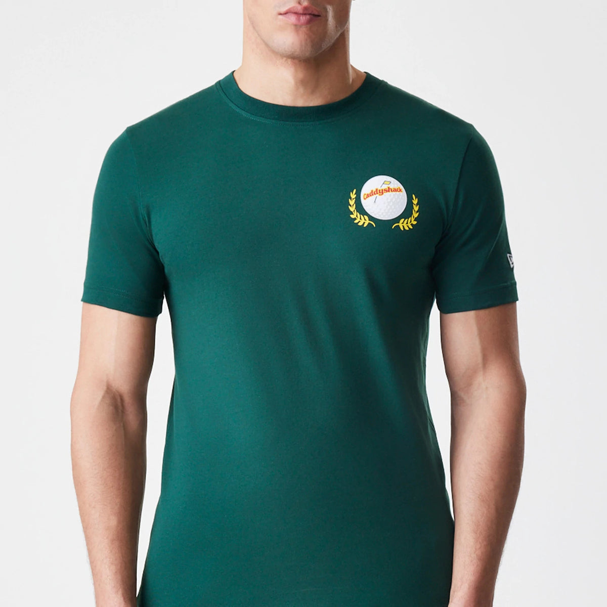 New Era Caddyshack It's In The Hole Dark Green T-Shirt, front view showing a round emblem with a golf ball and laurel design on the left chest, a small raised New Era logo on the left sleeve.