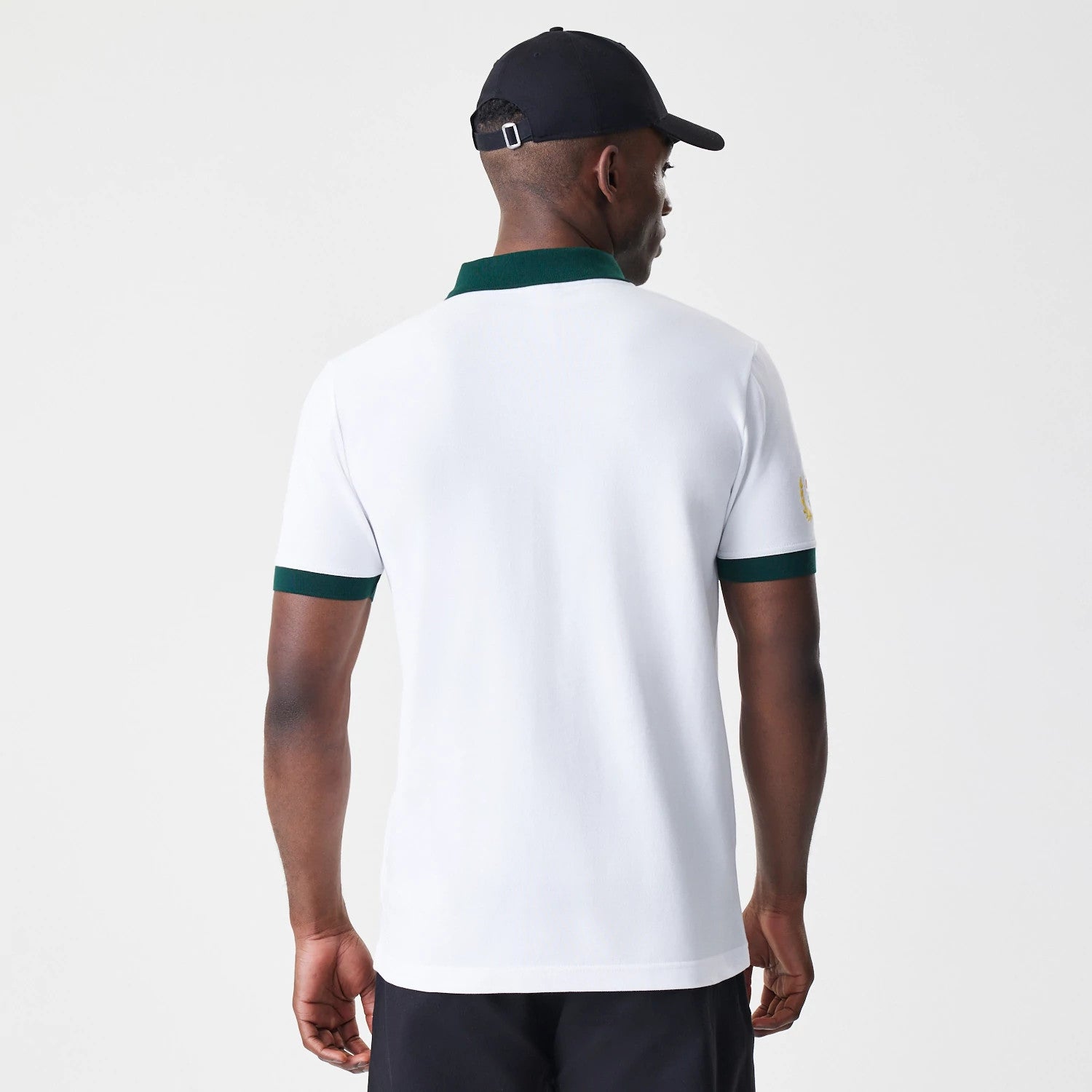 New Era Caddyshack BushWood White Polo T-Shirt, rear view showing a plain white back with dark green collar and sleeve cuffs, a small raised logo on the left sleeve, and the shirt worn by a model with a black cap.
