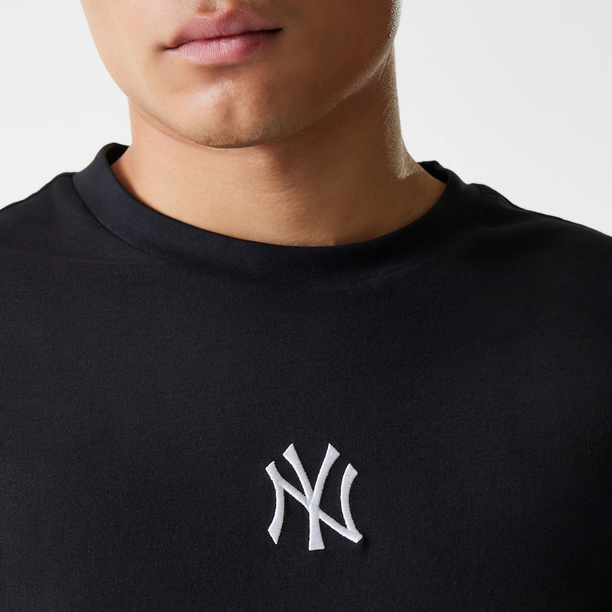 New Era New York Yankees MLB League Essential Black Oversized T-Shirt, front view showing the black fabric with a raised white New York Yankees logo on the chest, featuring a round neckline and short sleeves.
