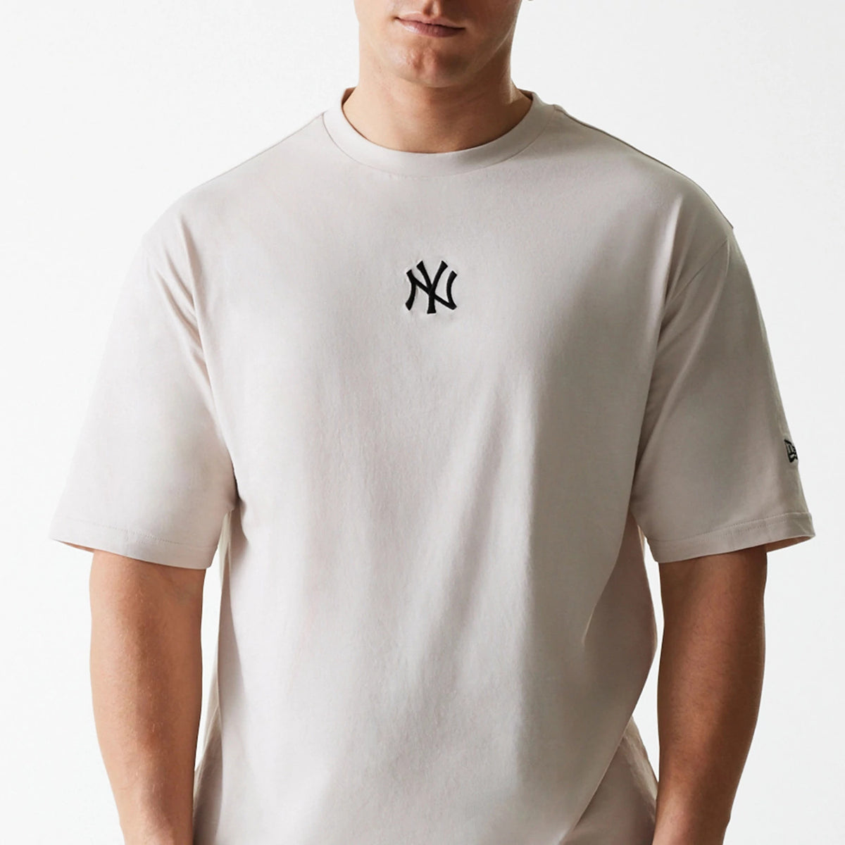 New Era New York Yankees MLB League Essential Cream Oversized T-Shirt, front view showing a cream T-shirt with a raised black NY logo on the chest and a small New Era logo on the left sleeve near the hem.