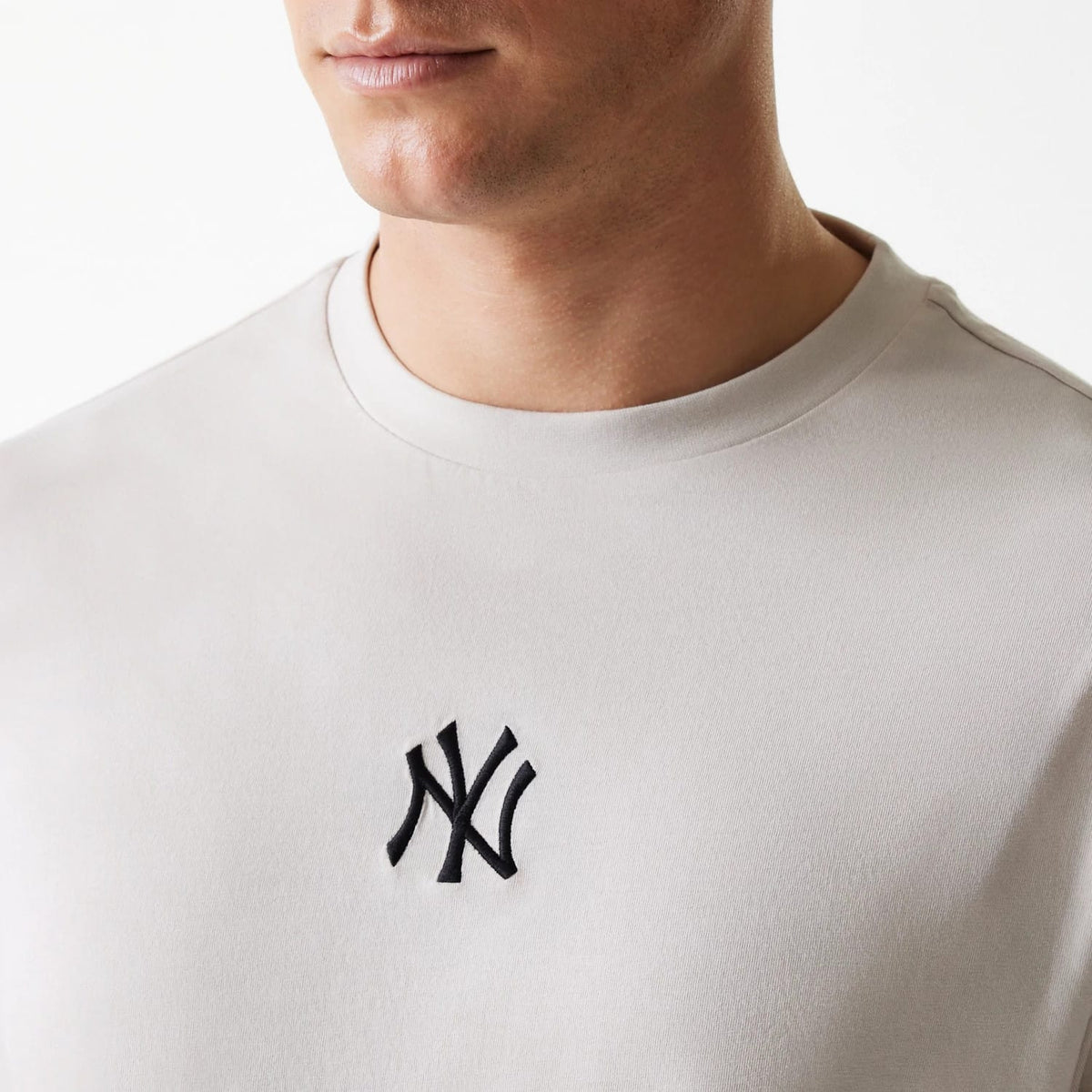 New Era New York Yankees MLB League Essential Cream Oversized T-Shirt, front view showing a raised black NY logo centred on the chest below the round neckline of the cream oversized shirt.