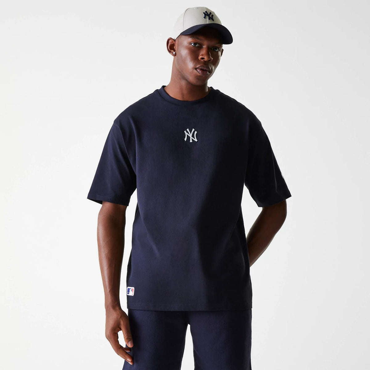 New Era New York Yankees MLB League Essential Navy Oversized T-Shirt, front view showing a white New York Yankees logo centred on the chest, short sleeves, and a relaxed fit, worn by a model wearing a navy and cream baseball cap.