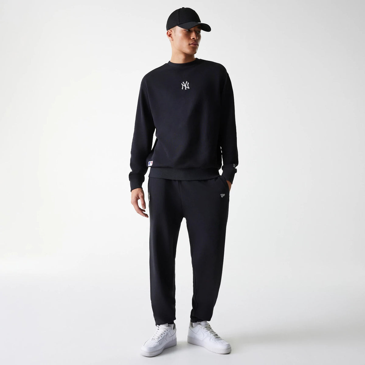 New Era New York Yankees MLB League Essential Midi French Terry Black Joggers, on a model styled with a coordinating black sweatshirt and cap, featuring an embroidered New Era flag logo near the left pocket.