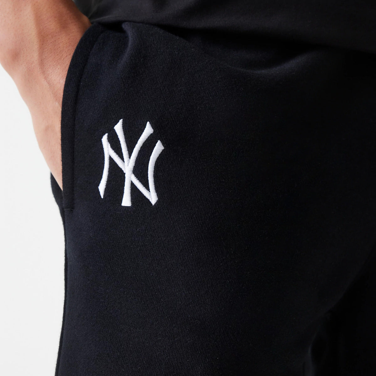 New Era New York Yankees MLB League Essential French Terry Black Shorts, side view showing the black fabric with an embroidered white NY logo on the upper thigh near the pocket opening.