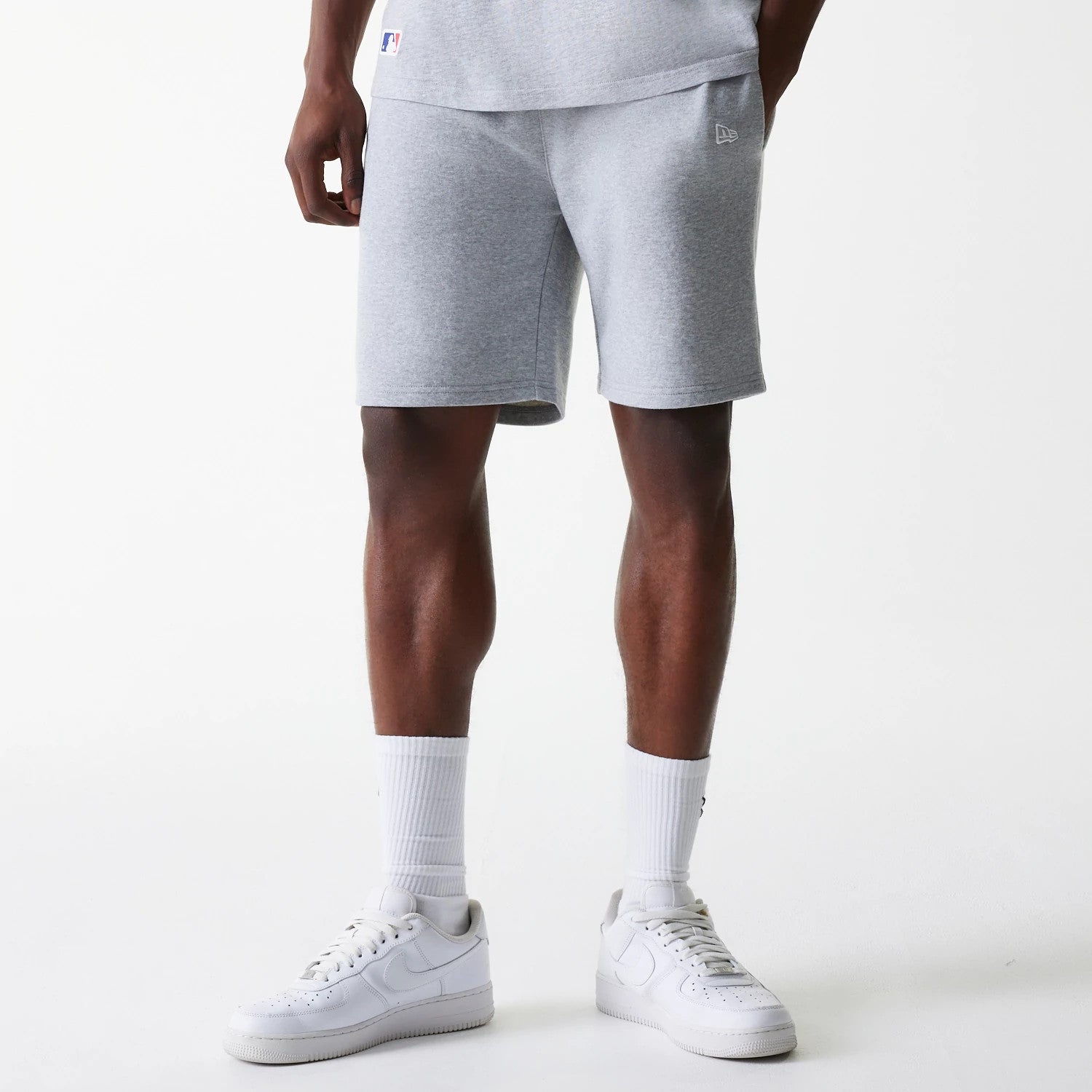 New Era New York Yankees MLB League Essential French Terry Grey Shorts, front view showing the soft grey fabric with a raised New Era logo on the left thigh, the shorts end above the knee and pair with white trainers and socks.