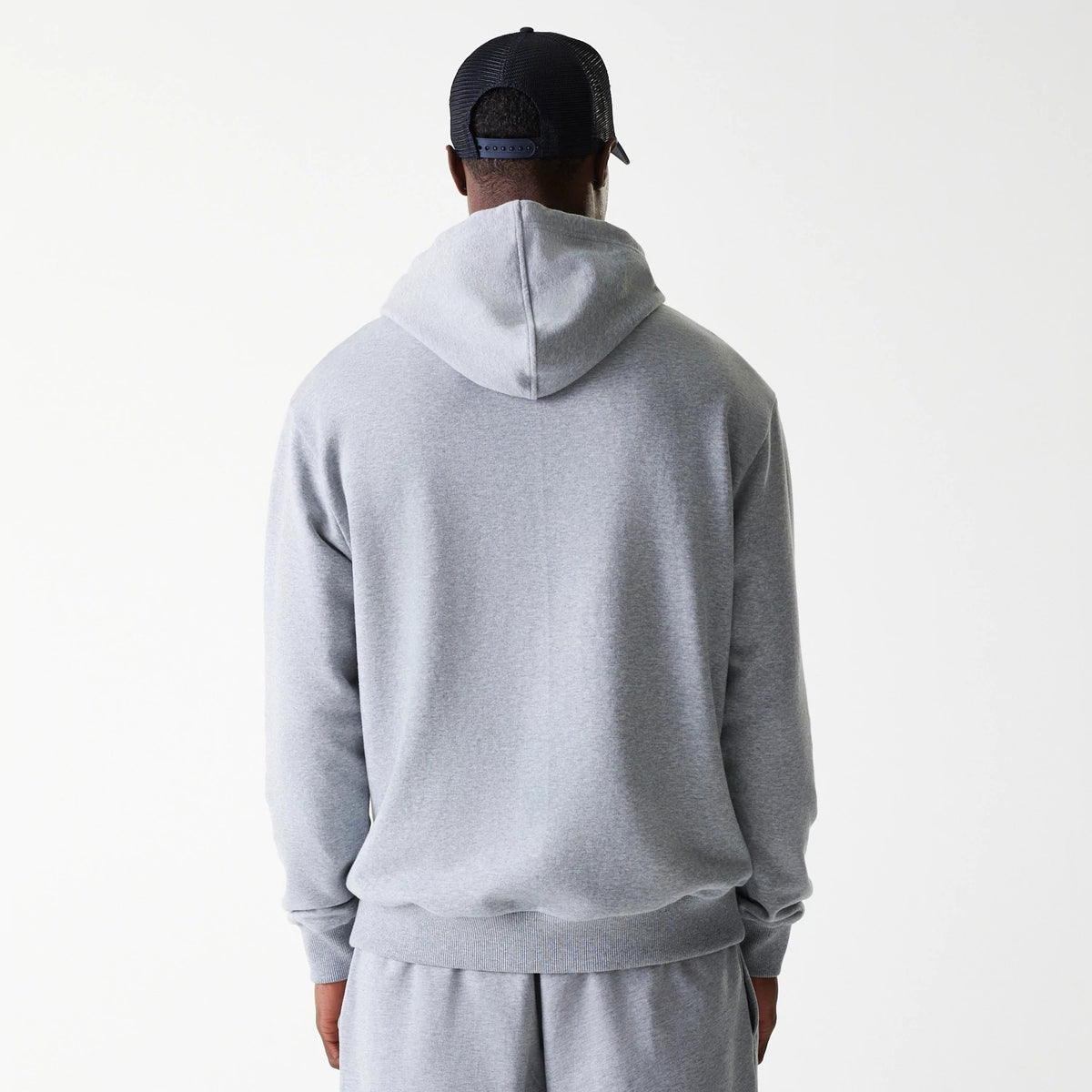 New Era New York Yankees MLB League Essential Midi French Terry Grey Oversized Pullover Hoodie, rear view showing the plain grey back with a relaxed hood, long sleeves, and ribbed hem, worn by a person in matching grey trousers.