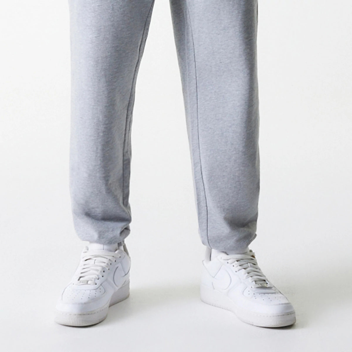 New Era New York Yankees MLB League Essential Midi French Terry Grey Joggers, close-up on a model showing the lower legs and hems paired with white trainers, highlighting the slim fit and soft grey fabric texture.