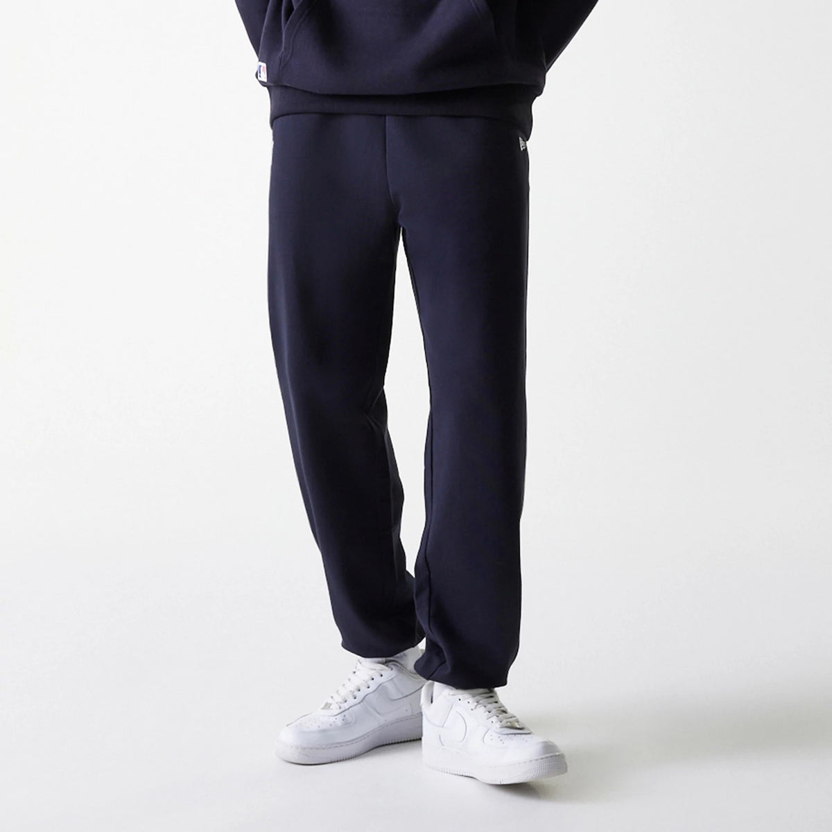 New Era New York Yankees MLB League Essential Midi French Terry Navy Joggers, front view on a model wearing white trainers, showing a relaxed tailored fit with side pockets and small embroidered Yankees logo near the left hip.