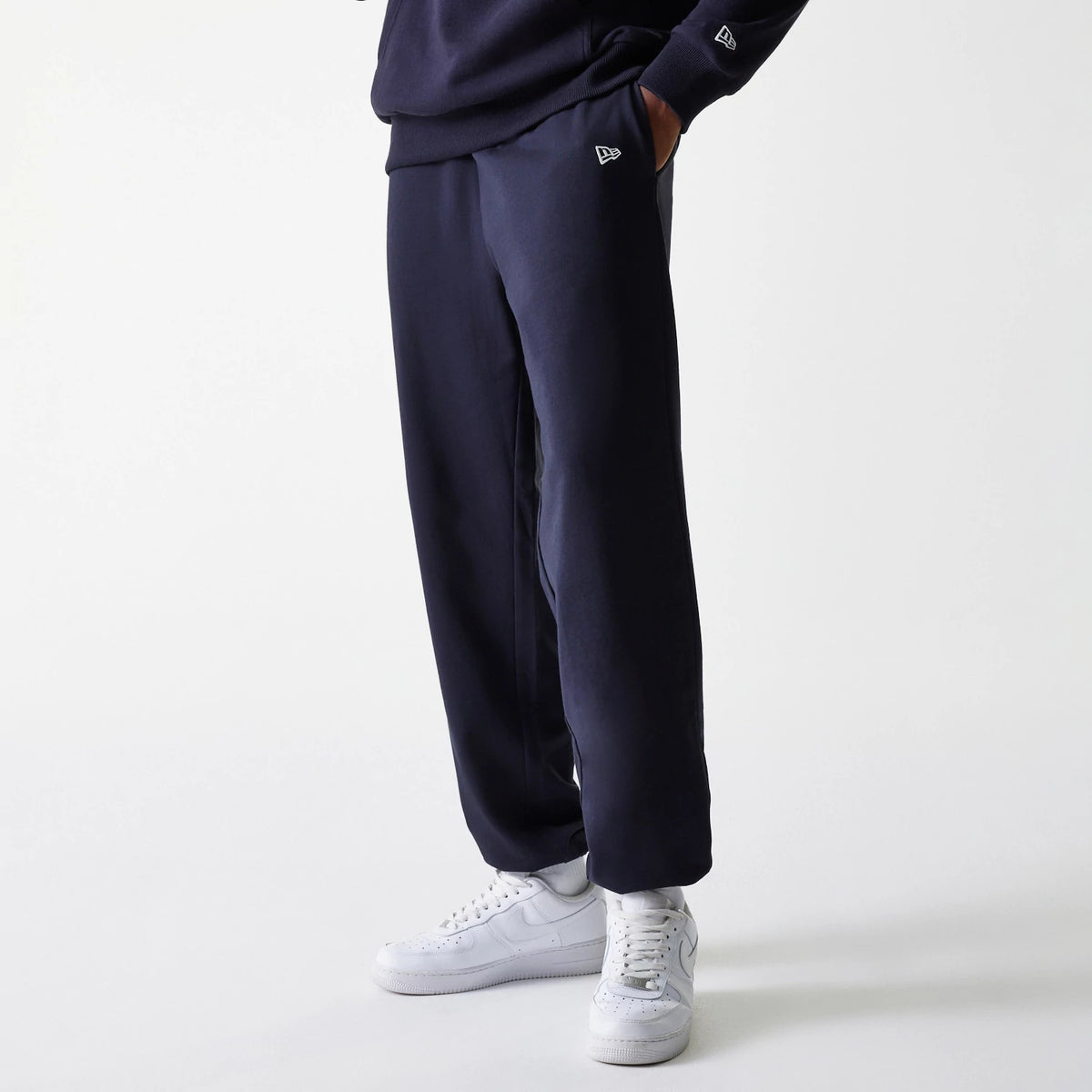 New Era New York Yankees MLB League Essential Midi French Terry Navy Joggers, on a model showing the relaxed fit with side pockets, elastic waistband, and white New Era flag logo on the left thigh.