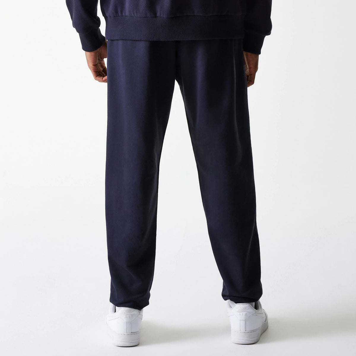 New Era New York Yankees MLB League Essential Midi French Terry Navy Joggers, back view on a model dressed in a matching navy sweatshirt and white trainers, showing the relaxed fit and elasticated waistband.