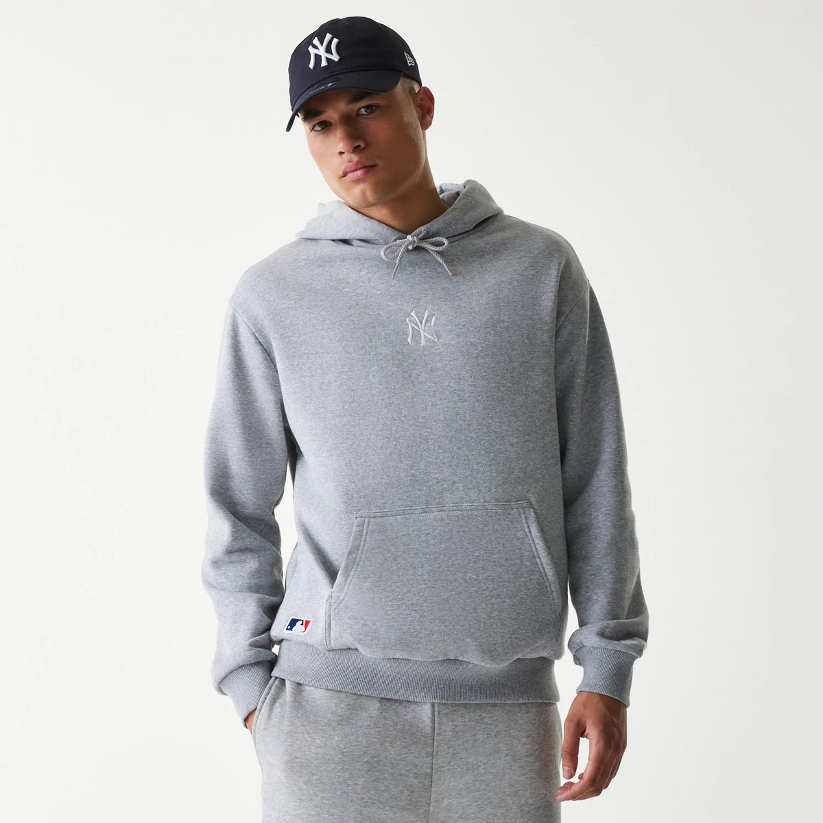 New Era New York Yankees MLB League Essential Grey Oversized Pullover Hoodie, front view showing a raised white Yankees logo on the chest, a kangaroo pocket, drawstrings on the hood and an MLB logo patch on the lower front.