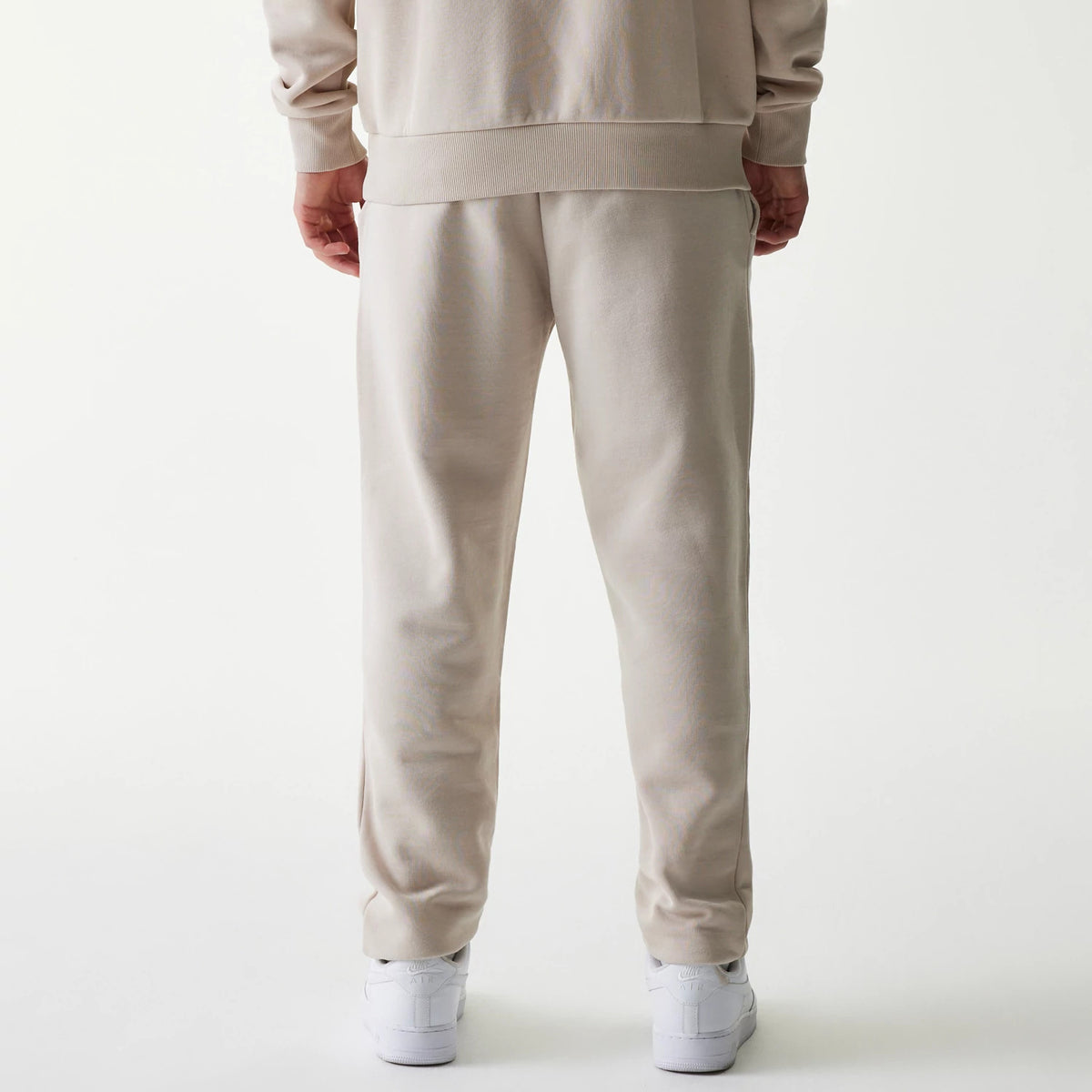 New Era New York Yankees MLB League Essential Cream Joggers, rear view on a model showing the relaxed fit with elasticated waistband and cuffs, paired with a matching cream sweatshirt and white trainers.