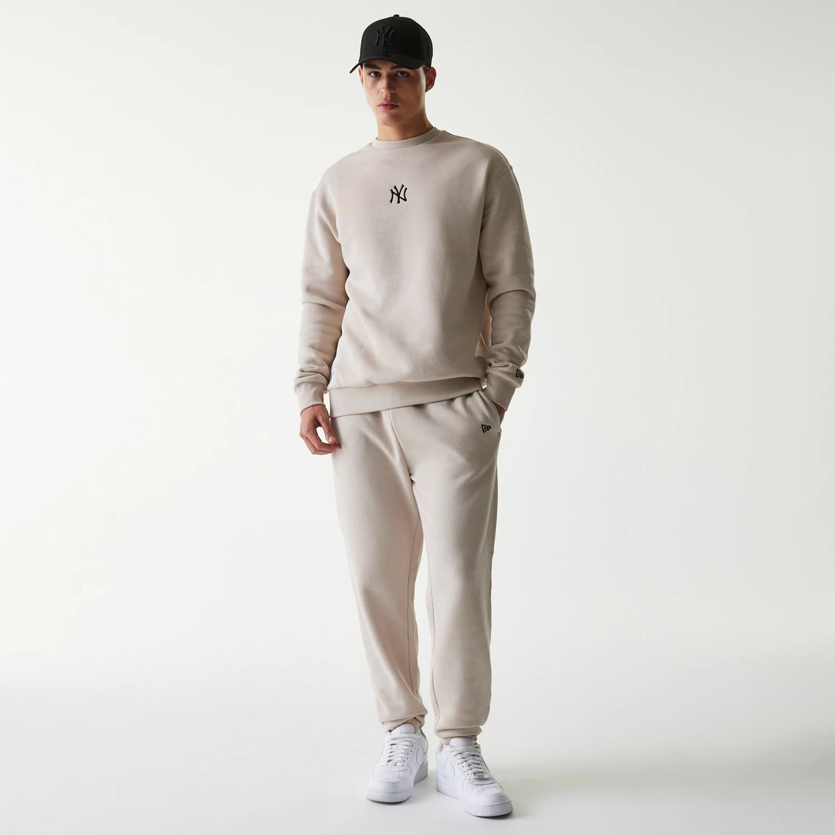 New Era New York Yankees MLB League Essential Cream Joggers, on a model styled with a cream sweatshirt and white sneakers, showing a small embroidered New Era flag logo near the left pocket and a relaxed fit.