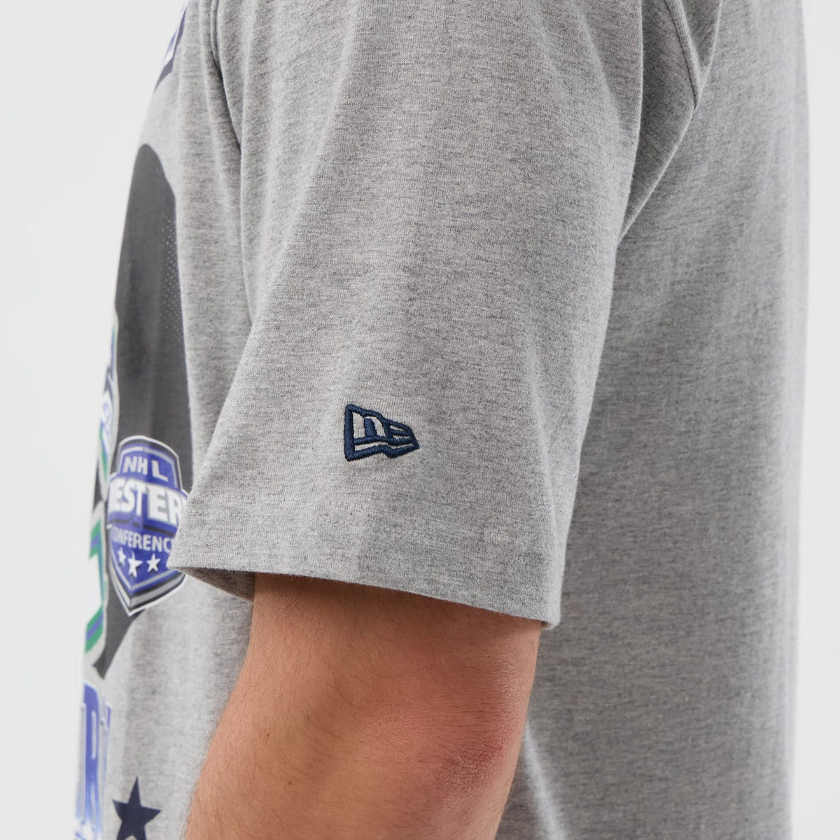 New Era Vancouver Canucks NHL Sport Classic Grey T-Shirt, side view showing the grey fabric of the sleeve with a raised New Era logo embroidered in blue near the hem and partial graphics visible on the side of the torso.