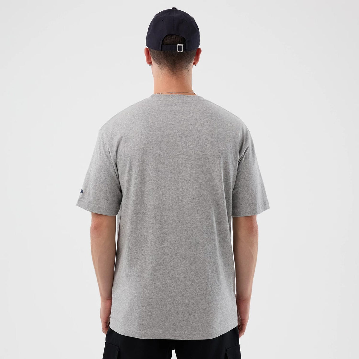 New Era Vancouver Canucks NHL Sport Classic Grey T-Shirt, rear view showing the plain grey back of the T-shirt, short sleeves and a small raised logo on the left sleeve, worn by a person also wearing a navy cap with eyelets.