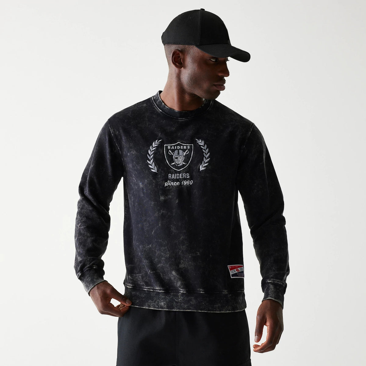 New Era Las Vegas Raiders NFL Throwback Black Crew Neck Sweater, front view on a model wearing a black cap, featuring the Raiders logo and laurels embroidered on the chest with Raiders Since 1960 text below.