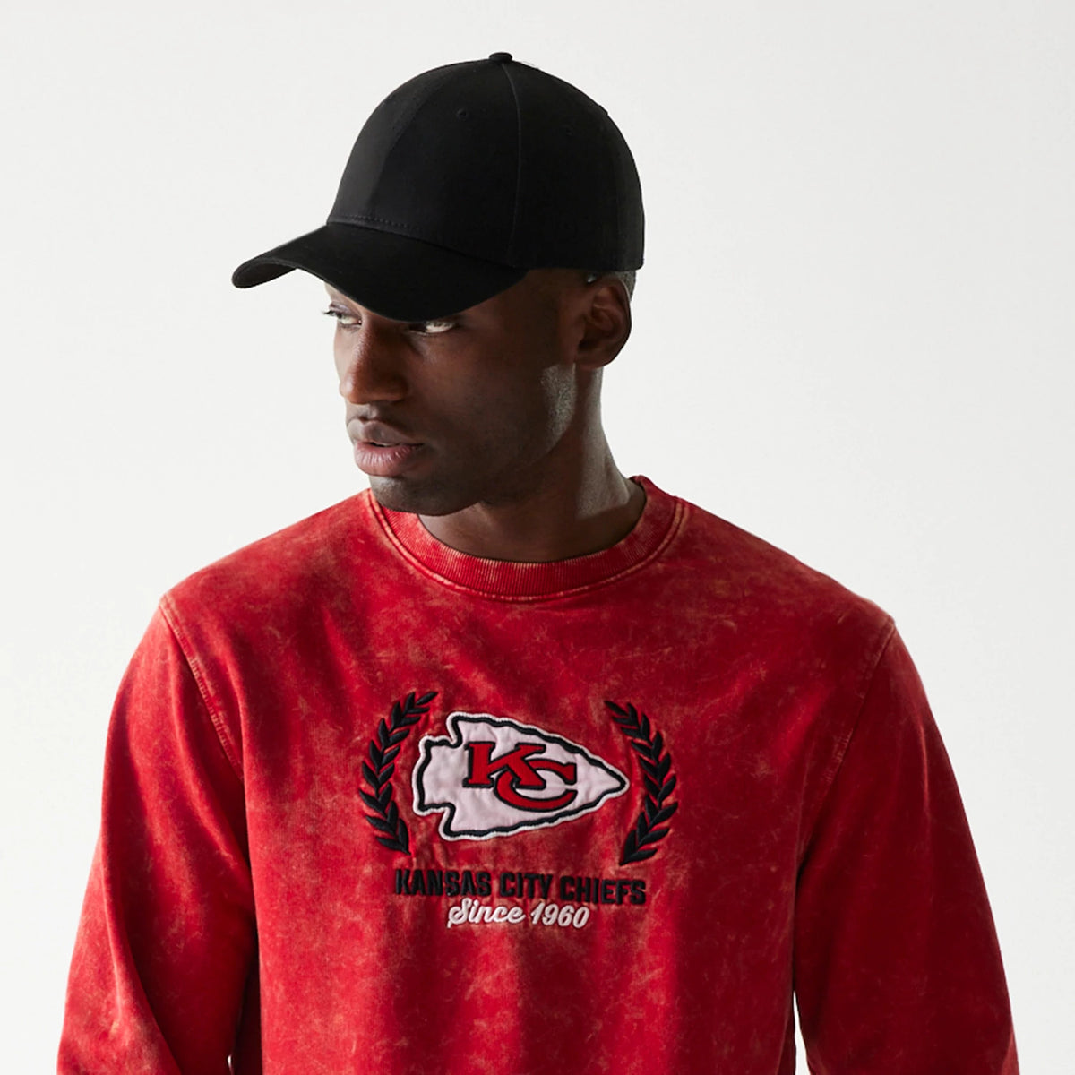 New Era Kansas City Chiefs NFL Throwback Red Crew Neck Sweater, on-model view showing a worn red finish with KC logo on the front chest, styled with a plain black cap on a model looking to the side.