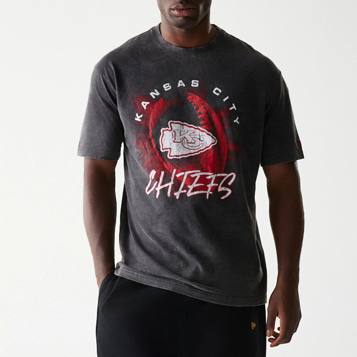 I don’t know who this person is, but here’s the alt text: Kansas City Chiefs NFL Sport Night Black T-Shirt, front view showing the faded black fabric with a large red and white Chiefs logo in the centre, surrounded by stylised text spelling Kansas City above and Chiefs below.