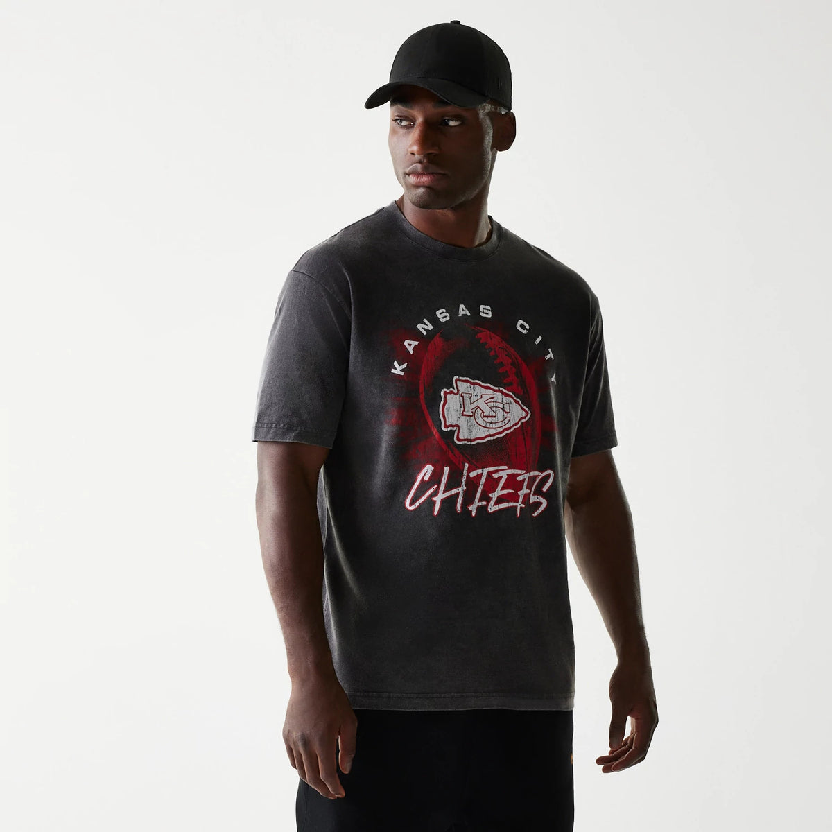 New Era Kansas City Chiefs NFL Sport Night Black T-Shirt, on-model view showing the front print with the team's logo centred within a stylised football, surrounded by red text and highlights on a black background, worn by a person.
