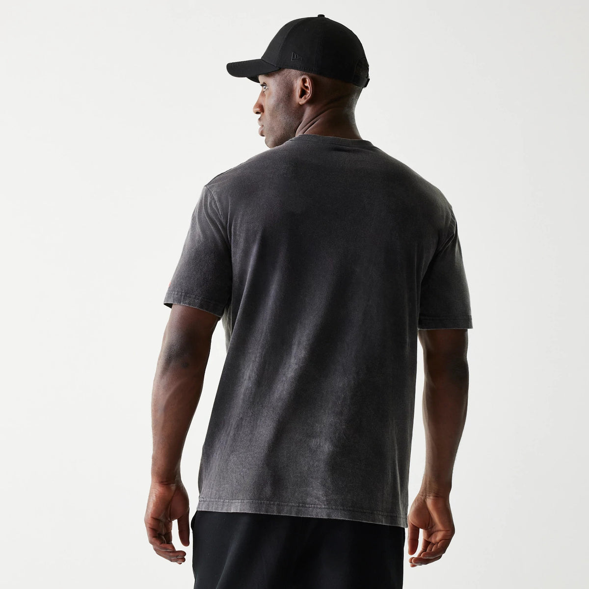New Era Kansas City Chiefs NFL Sport Night Black T-Shirt, on-model rear view showing the plain black back of the T-shirt with short sleeves, paired with a black cap featuring a debossed New Era logo on the side.