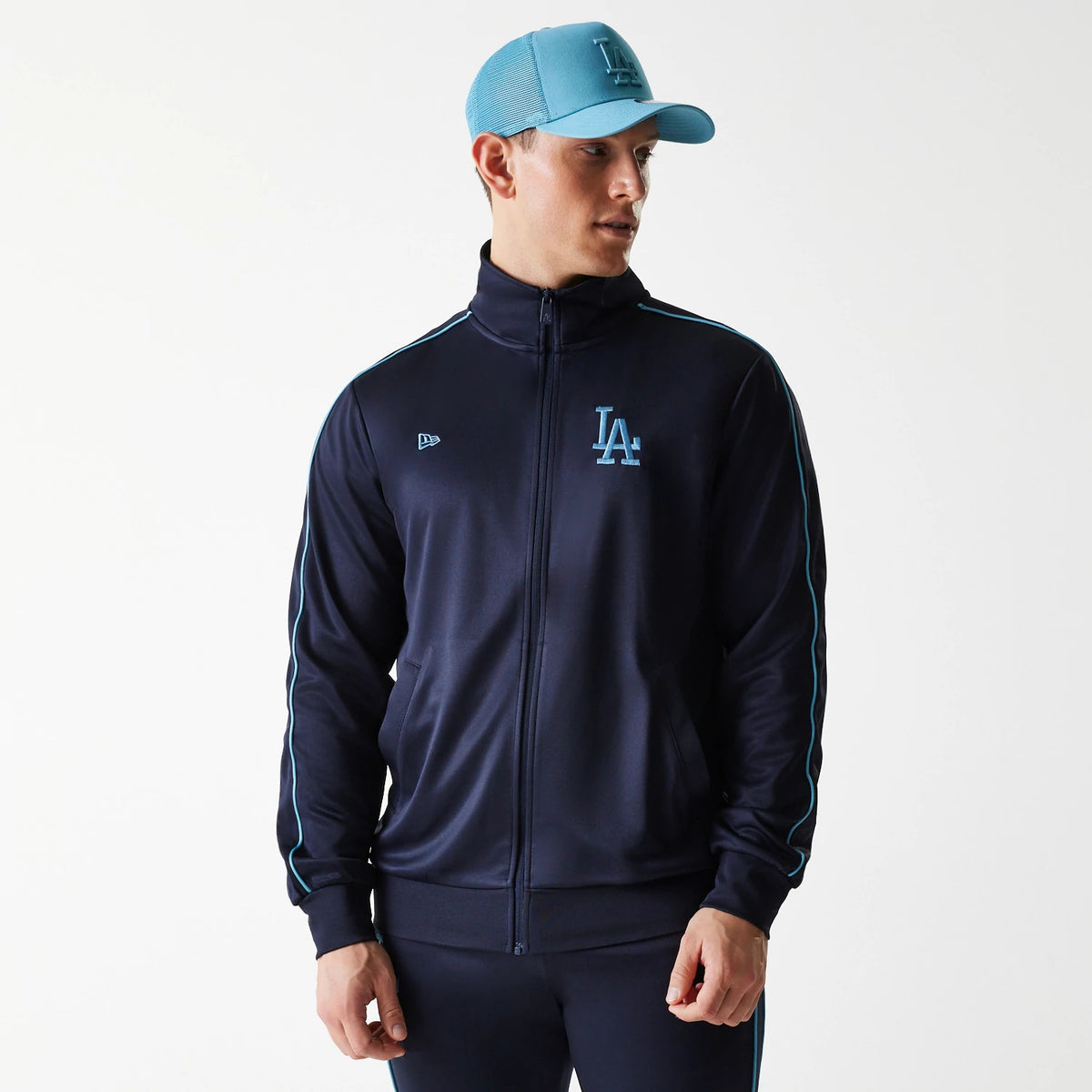 New Era LA Dodgers MLB Navy Track Top, on-model front view with a light blue LA logo on the left chest, light blue piping along the sleeves, and a matching cap featuring an LA logo and mesh panelling.