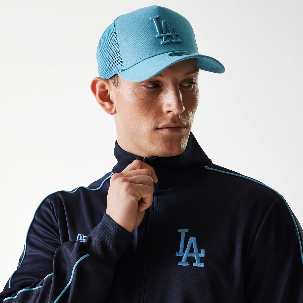 New Era LA Dodgers MLB Navy Track Top, on-model view with a matching blue cap featuring a raised LA logo on the front panel, showing the model adjusting the zip of the navy track top with sporty piping details.