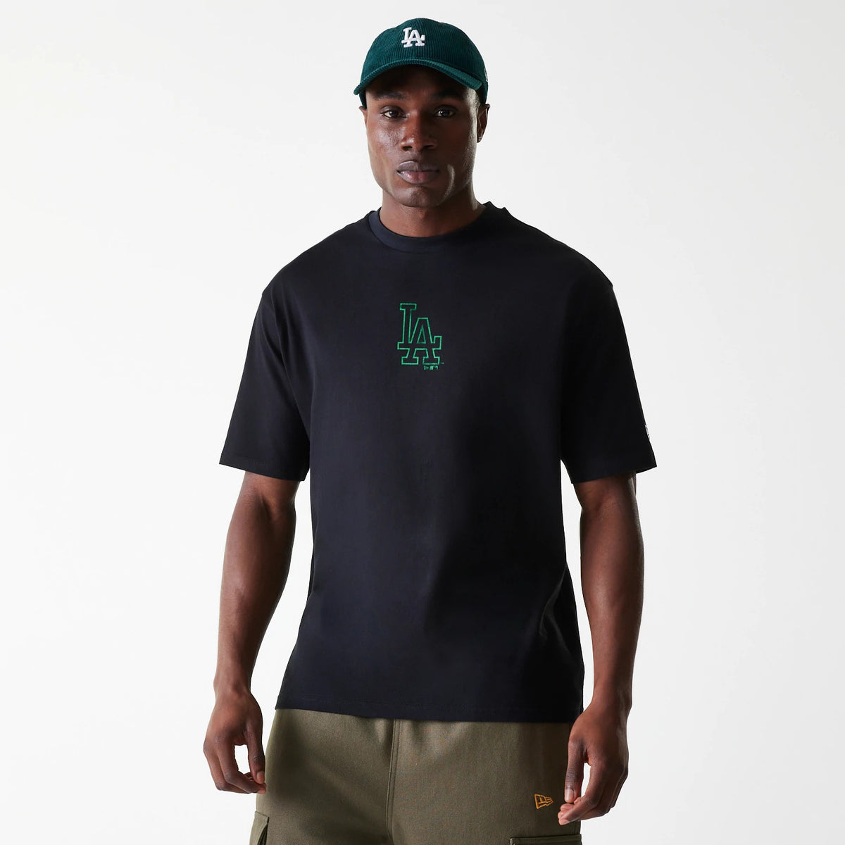 New Era LA Dodgers MLB World Series Black Oversized T-Shirt, on-model view showing the black t-shirt with a green LA logo centred on the chest, paired with a dark green cap featuring a white raised LA logo on the front.