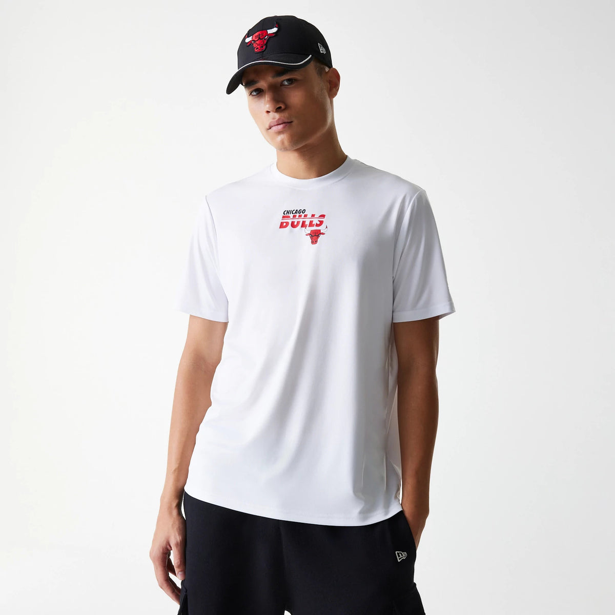 New Era Chicago Bulls NBA Essentials White T-Shirt, on-model view showing the white shirt with a red Bulls logo and text centred on the chest, paired with a black cap featuring an embroidered Bulls logo on the front.