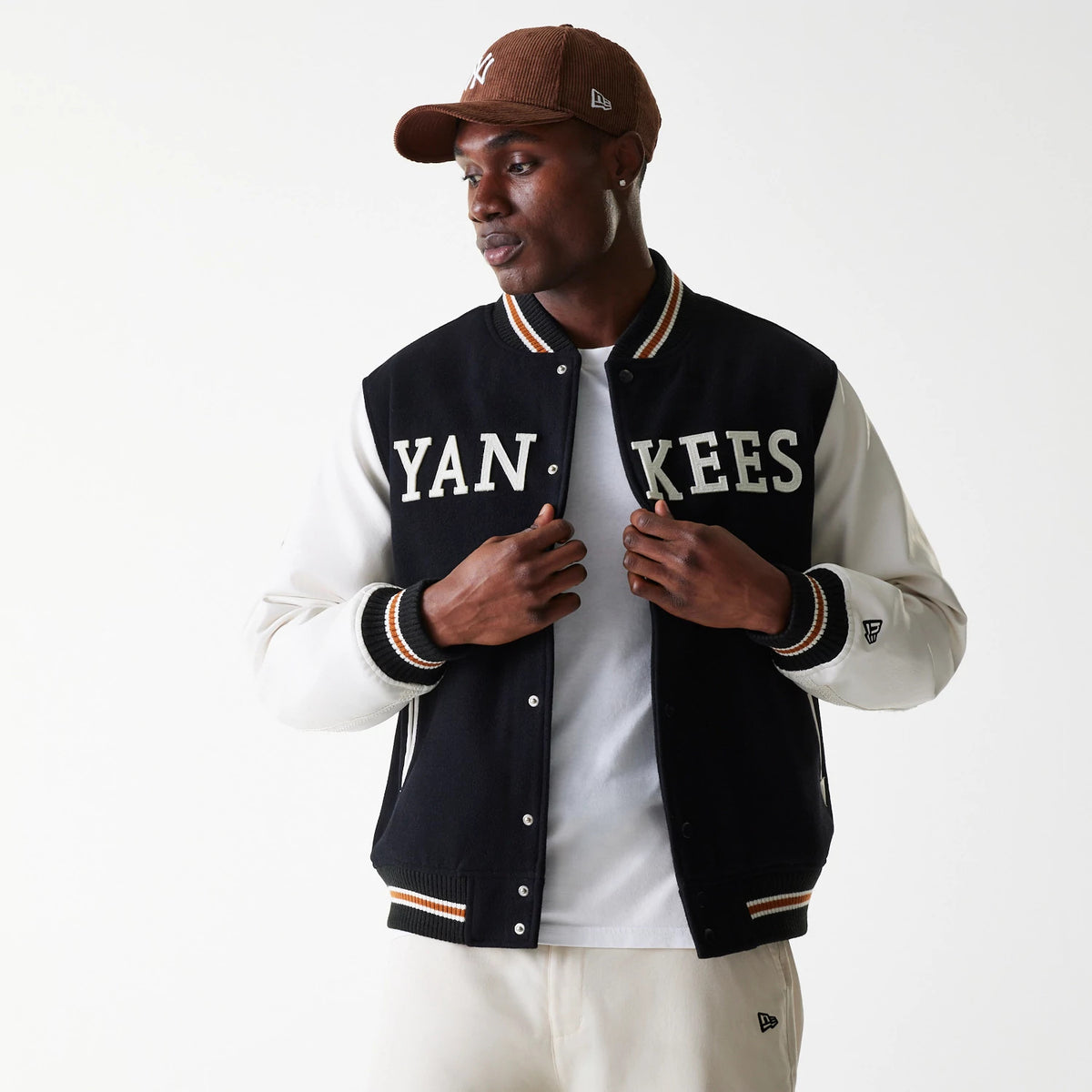 New Era New York Yankees MLB Wordmark Black Varsity Jacket, on-model view showing the black body with bold white YANKEES lettering across the chest, white sleeves, striped cuffs, and an embroidered New Era logo on the left sleeve.