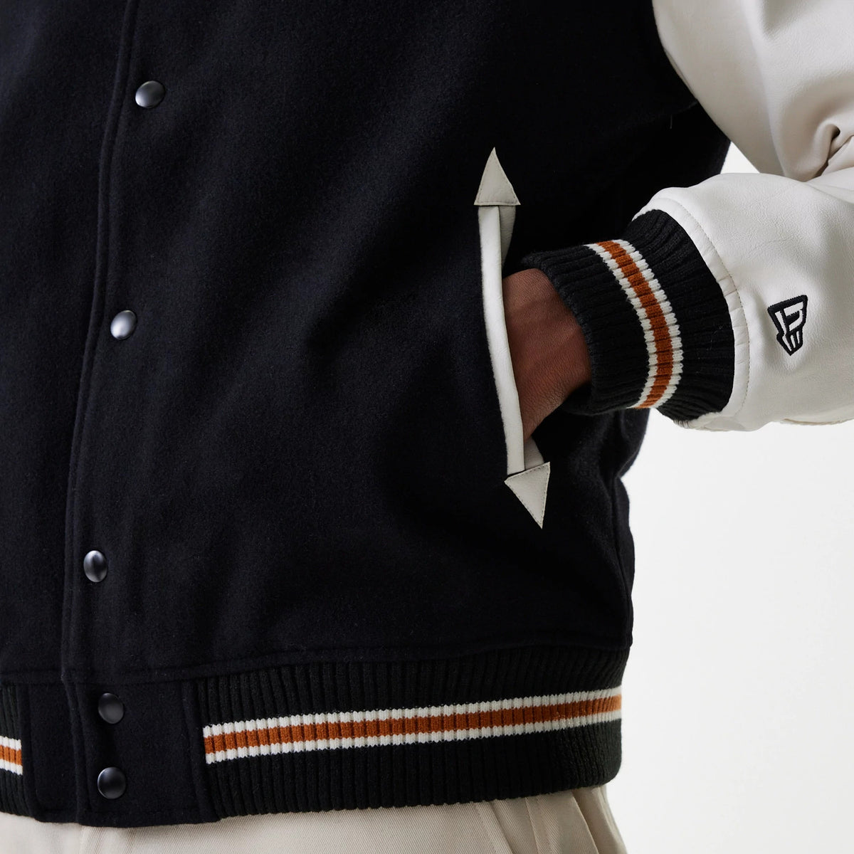 New Era New York Yankees MLB Wordmark Black Varsity Jacket, side view highlighting a debossed New Era logo on the left cream sleeve, black snap buttons along the front, black body with striped ribbed hem and cuffs, and white-trimmed pockets.