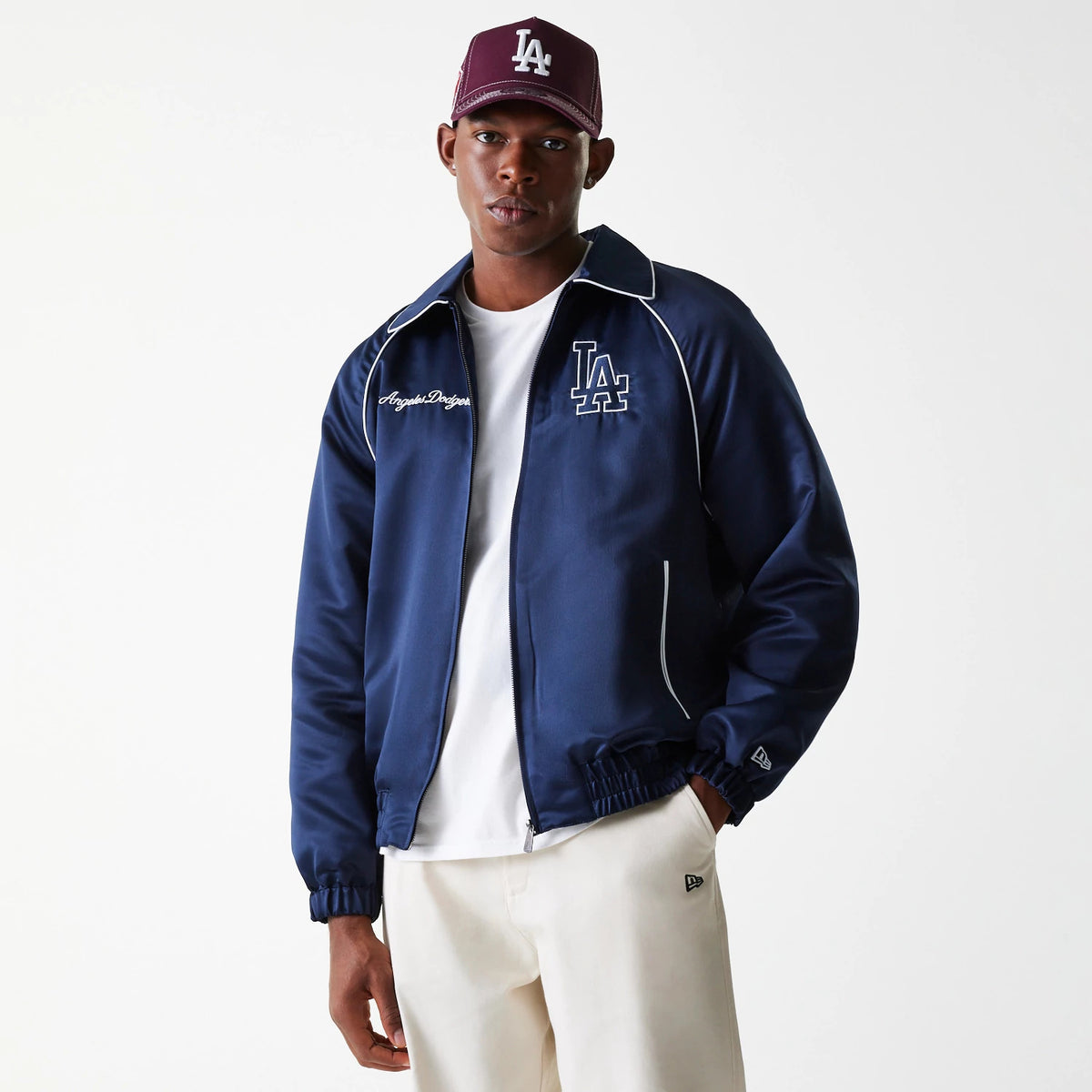 New Era LA Dodgers MLB Navy Club Jacket, on-model view showing the navy jacket with a white LA logo embroidered on the chest, white piping along the seams, and elasticated cuffs, worn over a white shirt with a burgundy LA logo cap.