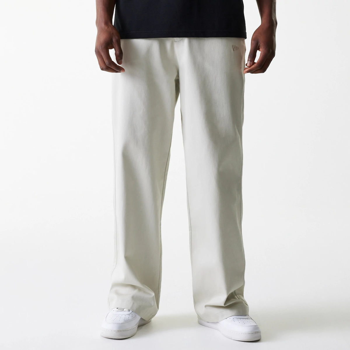 New Era New York Yankees MLB Light Beige Chino Trousers, front view on a model wearing a black top and white sneakers, showing the relaxed fit and the New Era flag logo embroidered on the left pocket area.