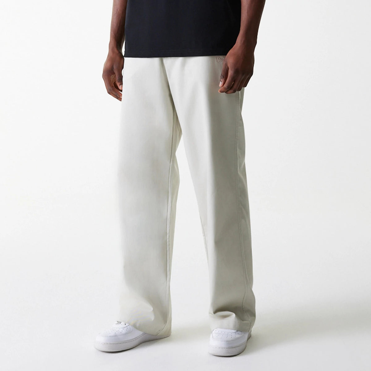 New Era New York Yankees MLB Light Beige Chino Trousers, front view on a model showing the relaxed straight-leg fit and crisp light beige colour, paired with a black T-shirt and white sneakers for a casual style.