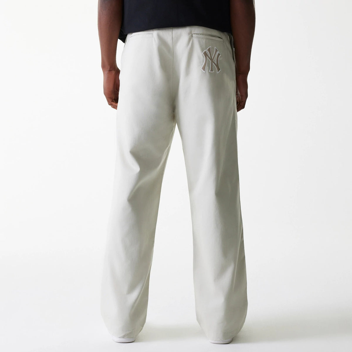 New Era New York Yankees MLB Light Beige Chino Trousers, rear view on a model showing the embroidered NY logo on the right pocket, set against the light beige fabric with a relaxed fit and straight leg design.
