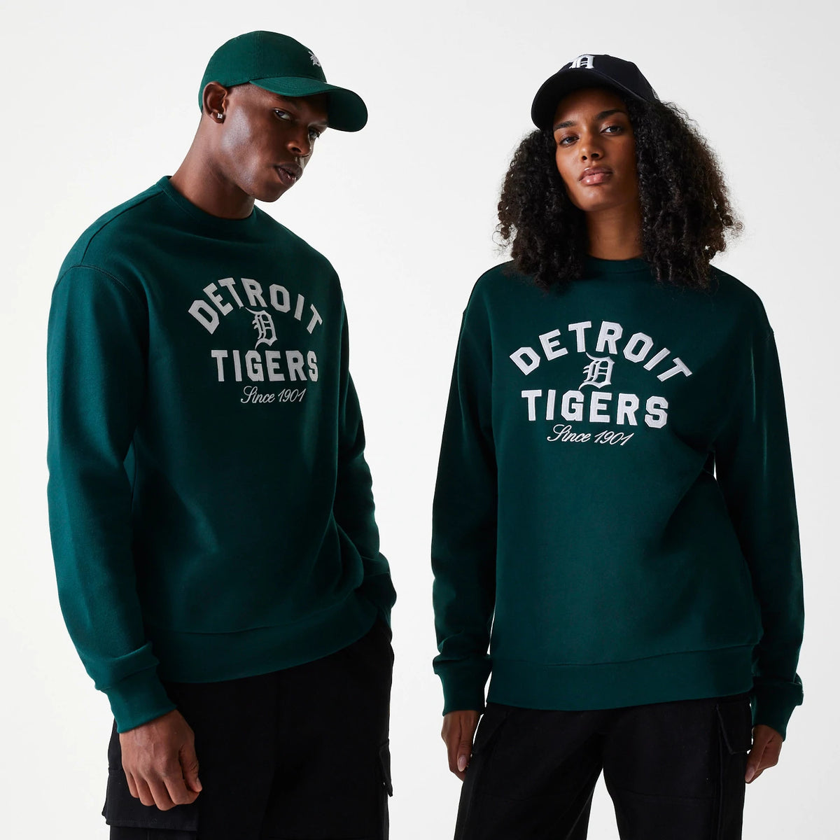 New Era Detroit Tigers MLB Heritage Dark Green Oversized Crew Neck Sweater, front view on a model and a matching cap, featuring embroidered white Detroit Tigers lettering and logo centred on the chest above Since 1901 script.