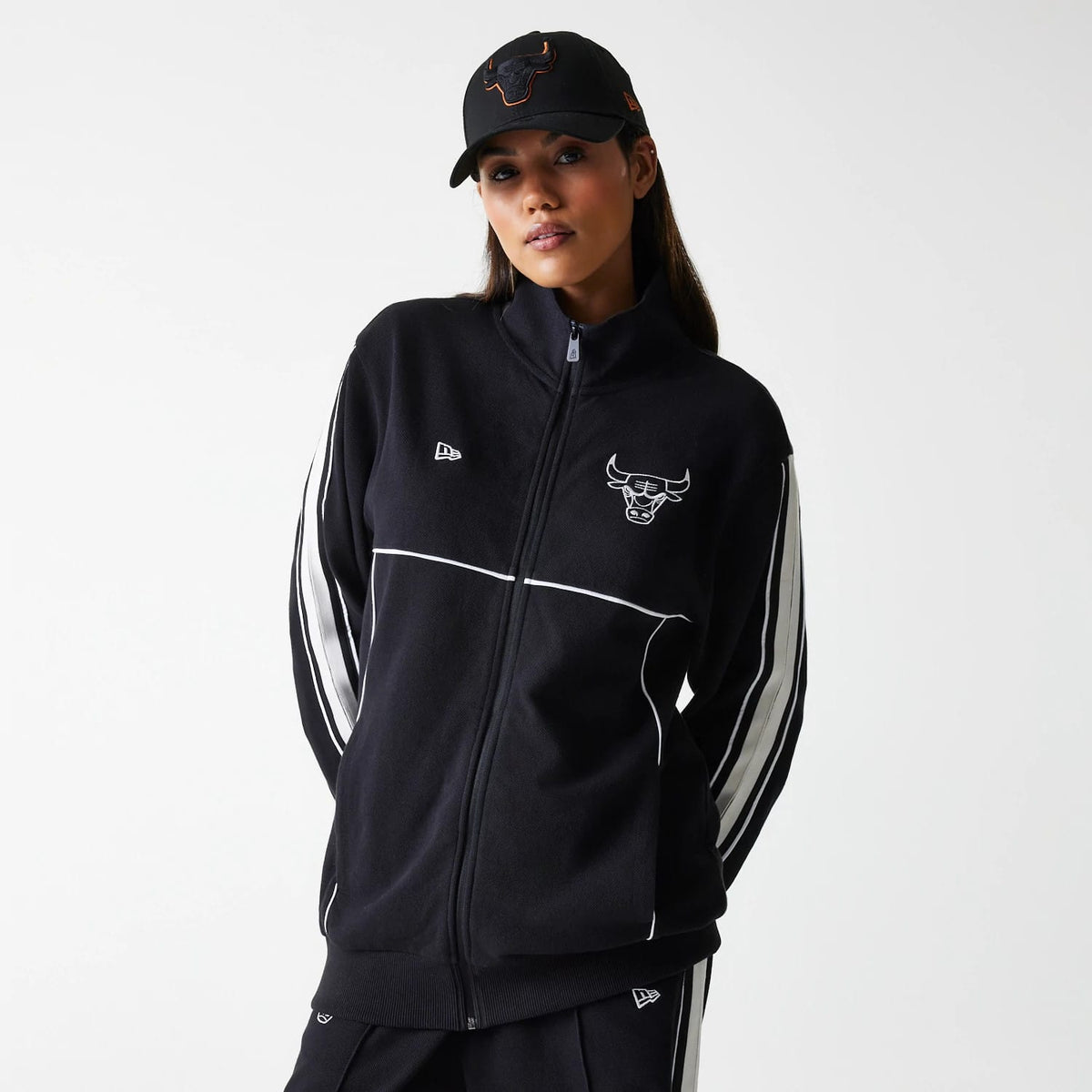 New Era Chicago Bulls NBA Outline Black Track Jacket, front three-quarter view showing a black shell with a raised Chicago Bulls logo on the chest, a raised New Era logo to the side, and white stripes running down the sleeves.