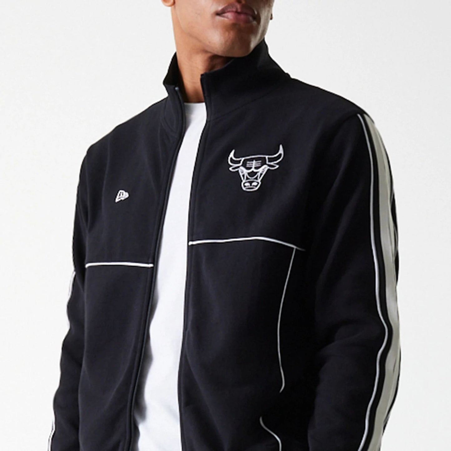 New Era Chicago Bulls NBA Outline Black Track Jacket, front view showing the black jacket with a raised Chicago Bulls logo on the left chest, a small raised New Era logo on the right chest, and white piping along the sleeves and chest.