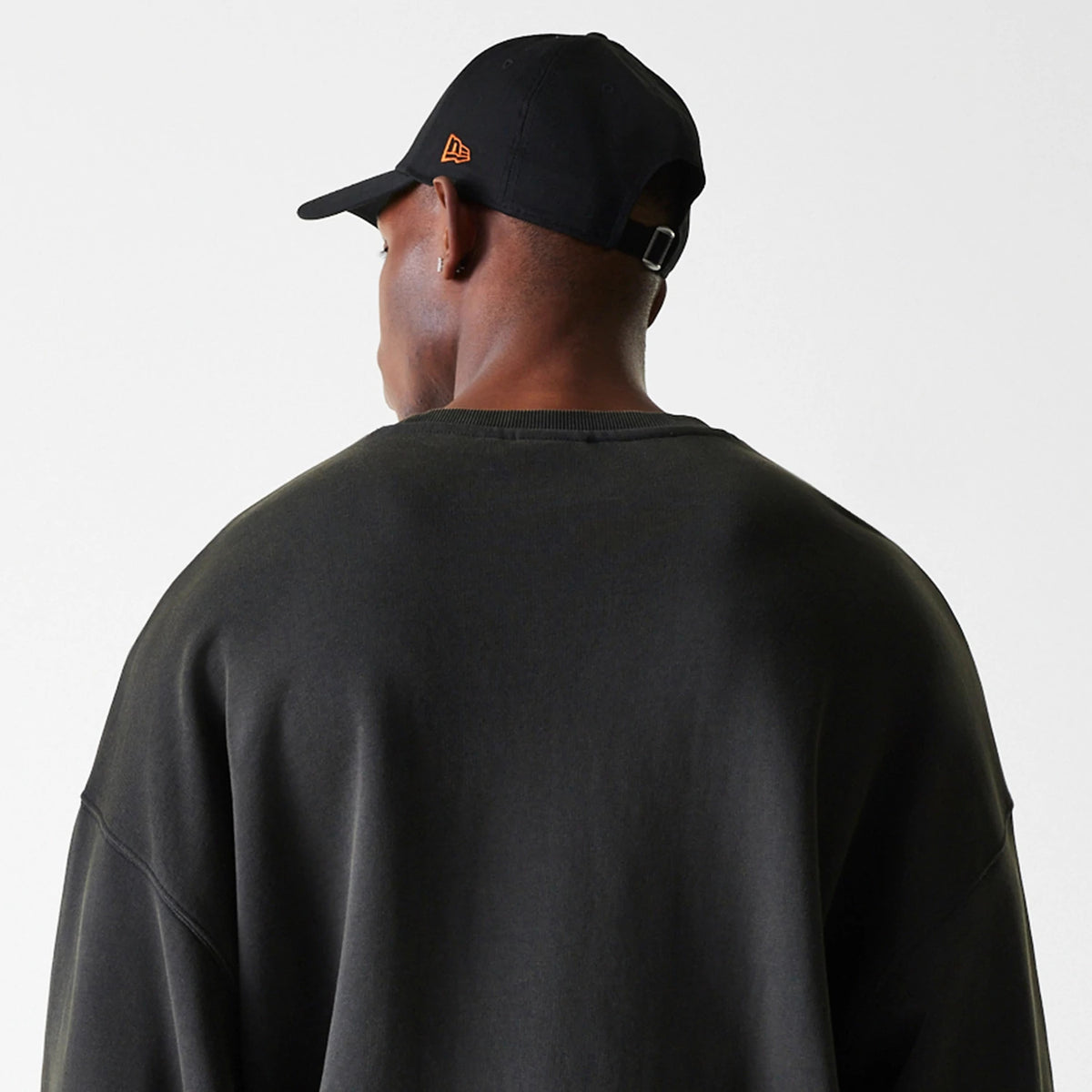 New Era Chicago Bulls NBA Washed Graphic Grey Oversized Crew Neck Sweater, rear view on a model with a black cap featuring an orange New Era flag logo on the left side, highlighting the relaxed fit and dropped shoulders.