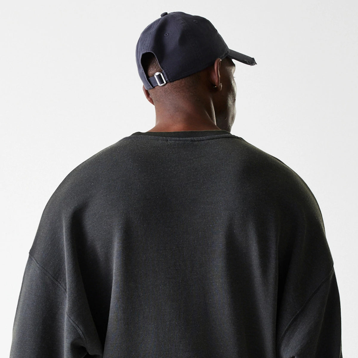 New Era LA Lakers NBA Washed Graphic Grey Oversized Crew Neck Sweater, rear view on a model styled with a navy cap, highlighting the loose fit and wide neckline of the grey sweater.